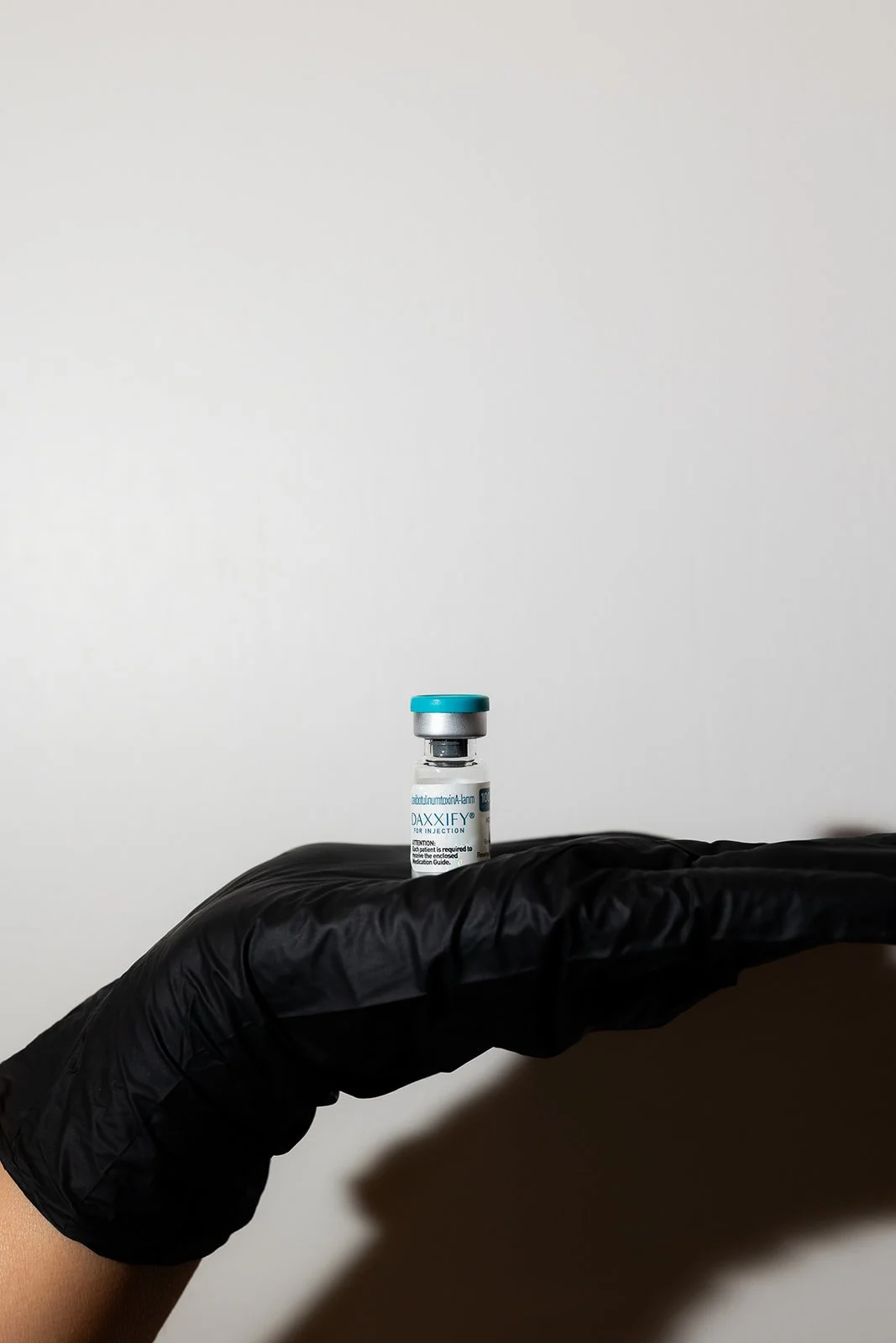 A gloved hand holding a small vial of vaccine or medication, against a plain background.