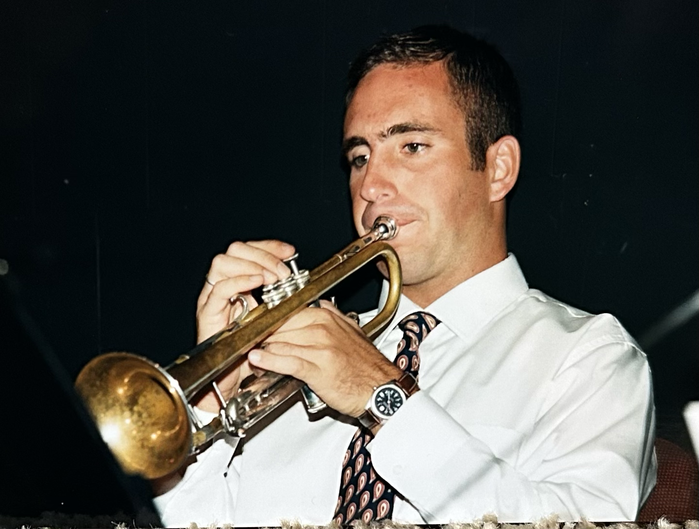 Man in a white shirt and patterned tie playing a trumpet.