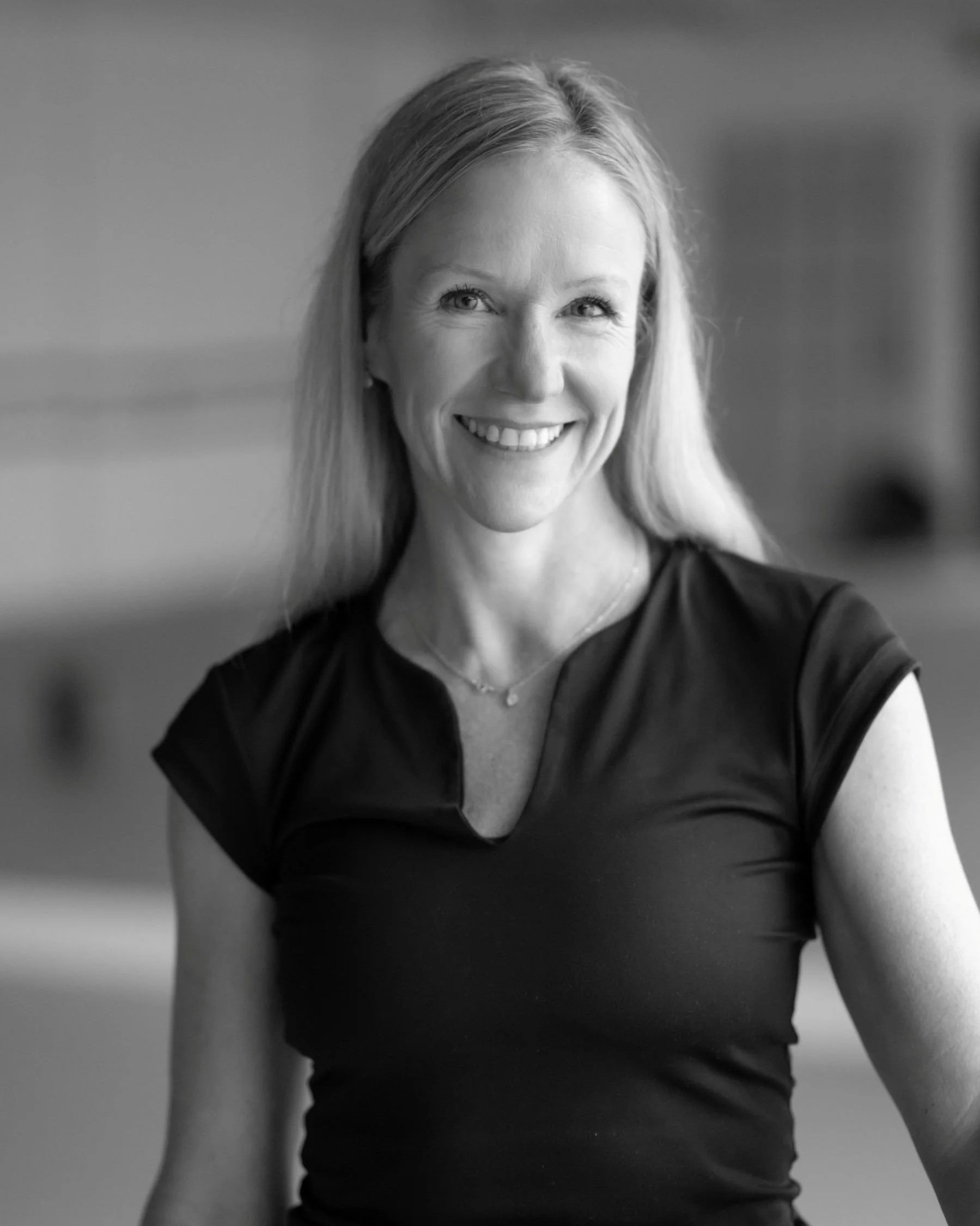 A smiling woman with long hair, wearing a dark top, looking at the camera.