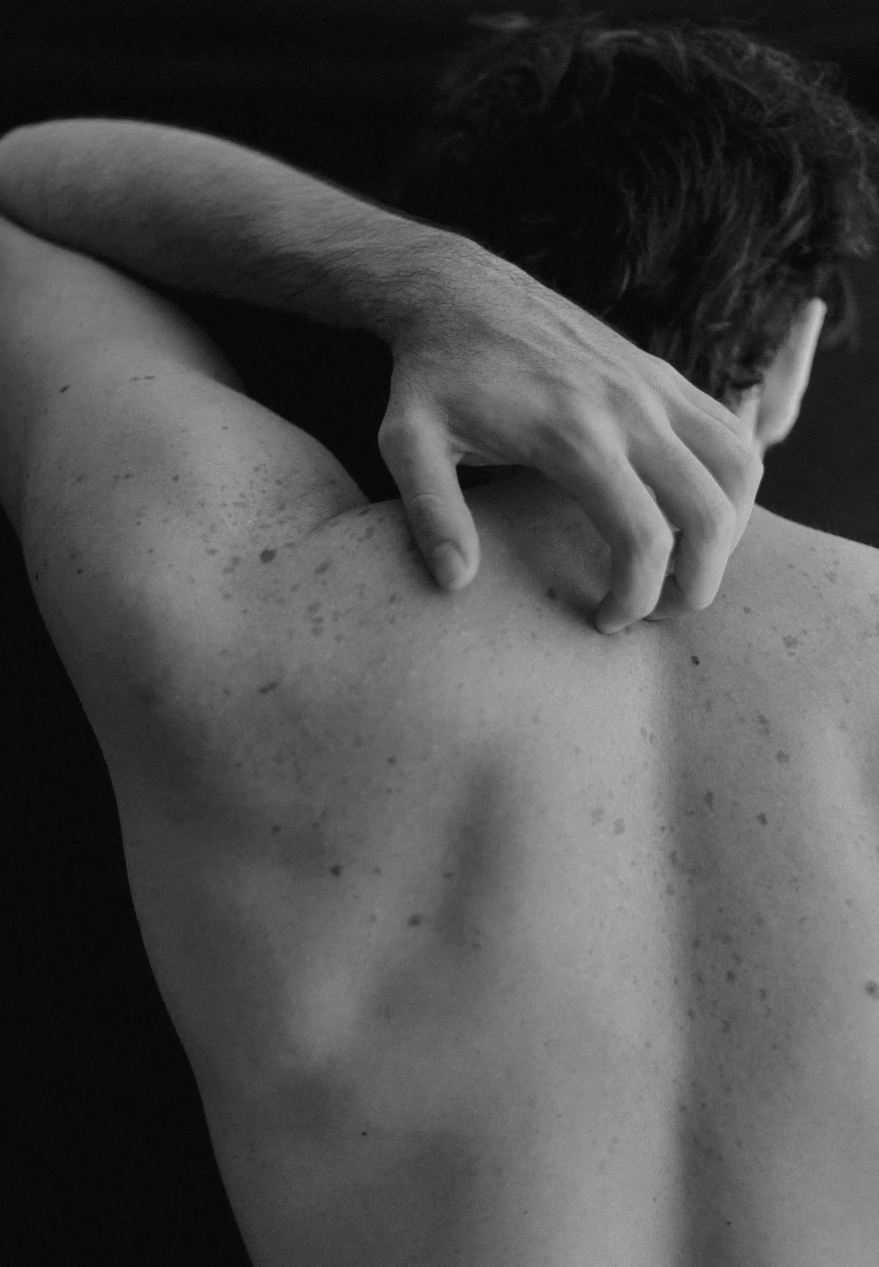 Black and white photo of a person's back and shoulder with a hand resting on it, their face turned away and partially obscured.