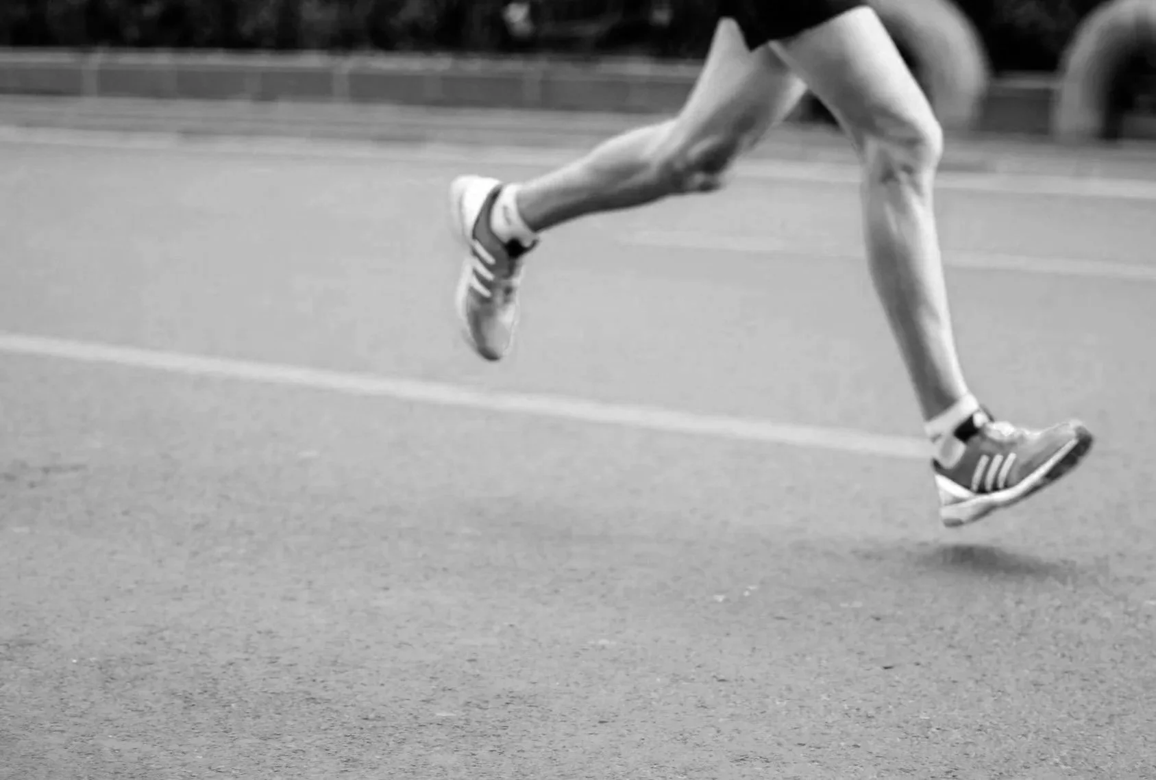 Close-up of a runner's legs and feet in motion on a track in black and white.