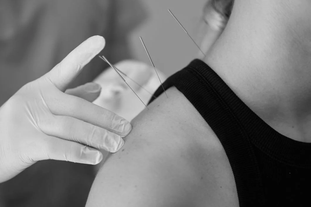 A person receiving an injection or vaccination in the upper arm, with medical gloves and multiple needles visible.