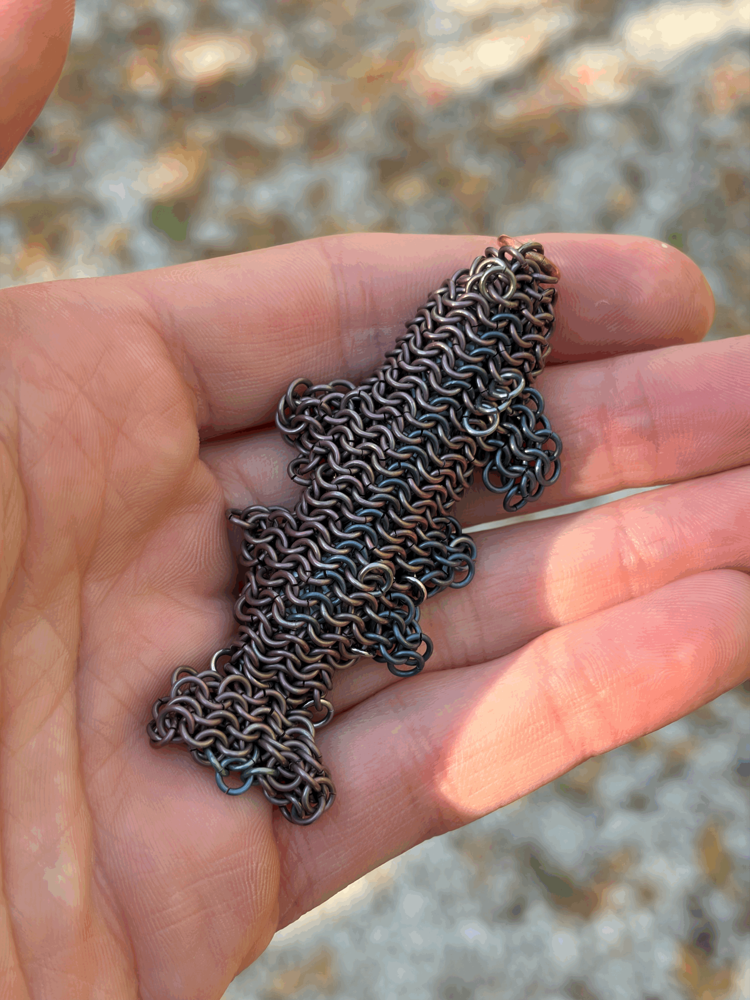 Titanium Trout contemporary metal fish sculpture by Emmit Flynn held in hand — palm-scale woven titanium trout amulet — Litor Studio