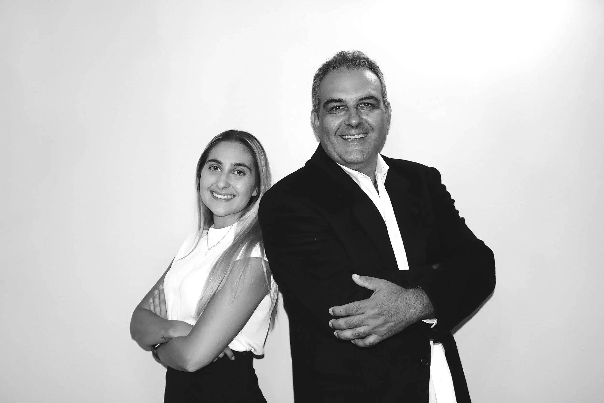 GTA real estate agents serving Oakville, Burlington, Milton, Mississauga, and Hamilton, standing back-to-back with arms crossed in a black and white portrait