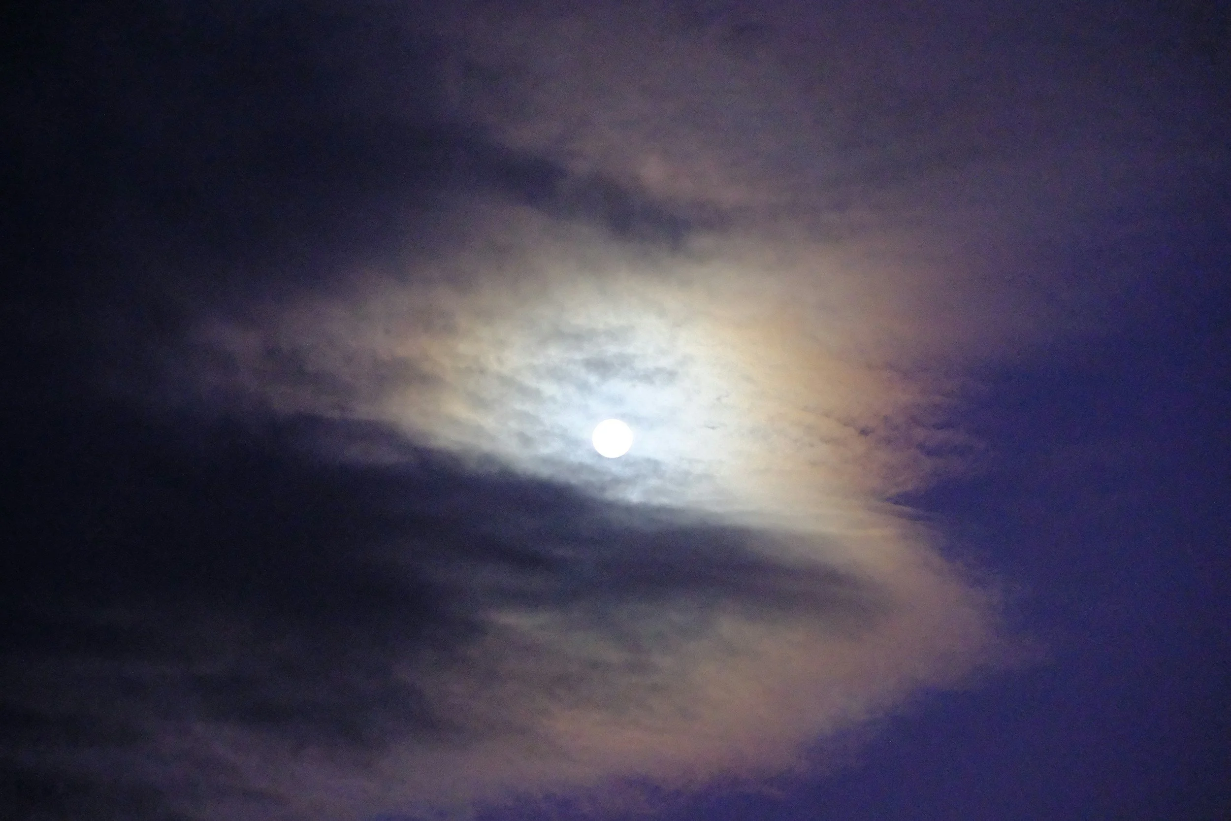 The image shows a bright full moon in the night sky, partially obscured by clouds illuminated by the moonlight, representing the transition into matrescence.