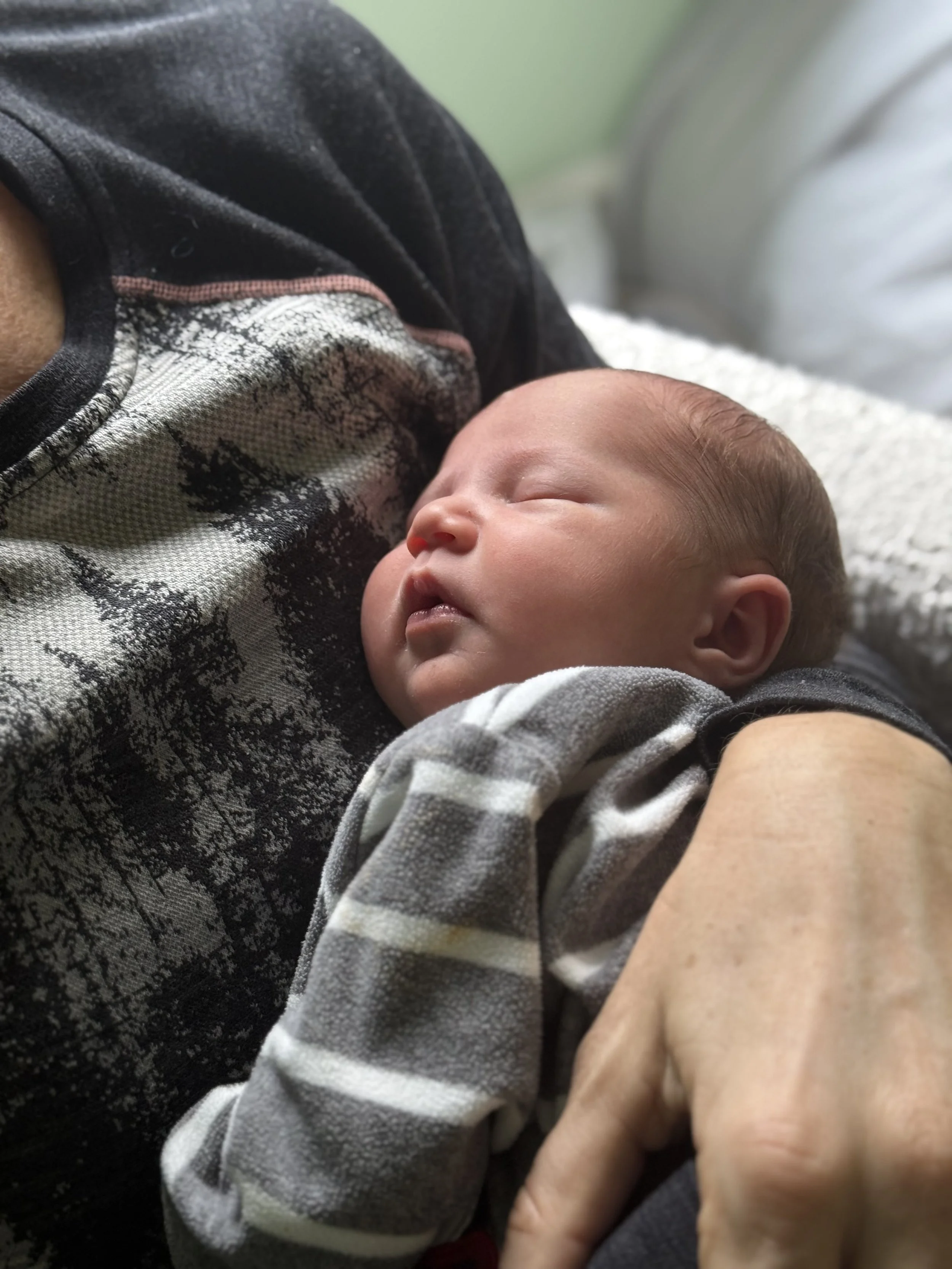 Close-up of a sleeping infant being held, wearing a striped shirt and covered with a blanket, with an adult's arm visible.