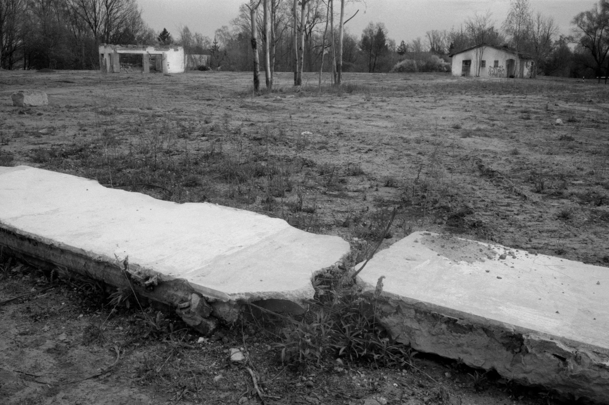 Dilapidated concrete sidewalk and abandoned buildings in a desolate outdoor area.