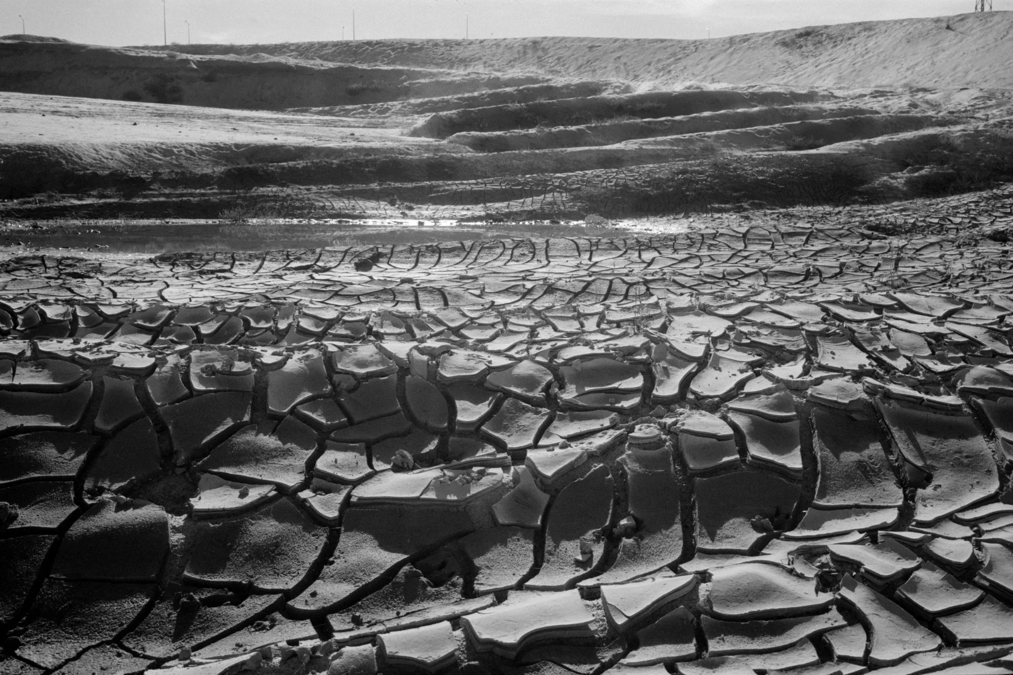 Dry, cracked earth in a barren landscape with distant hills and a clear sky.