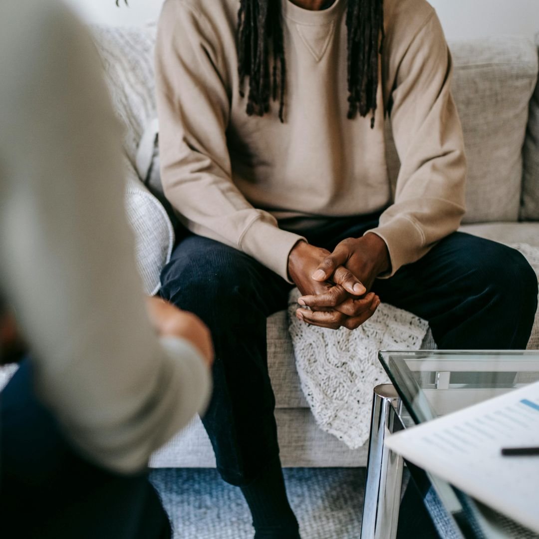 Persona seduta su un divano con le mani incrociate, visibilmente in una conversazione o consulto.