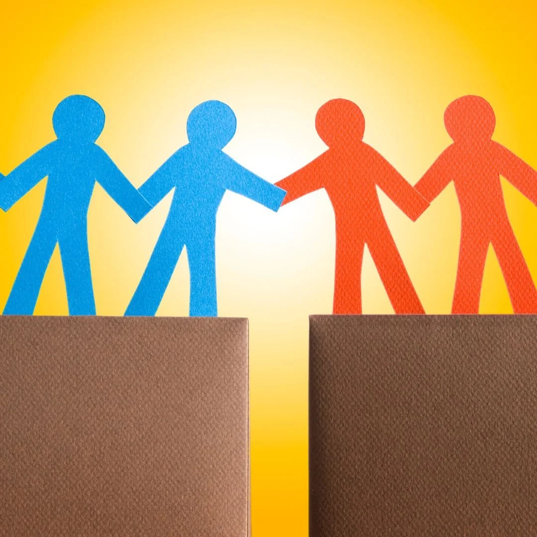 Figura di carta di due persone blu e due persone rosse che si tengono per mano e si trovano su blocchi di cartone, con uno sfondo giallo.