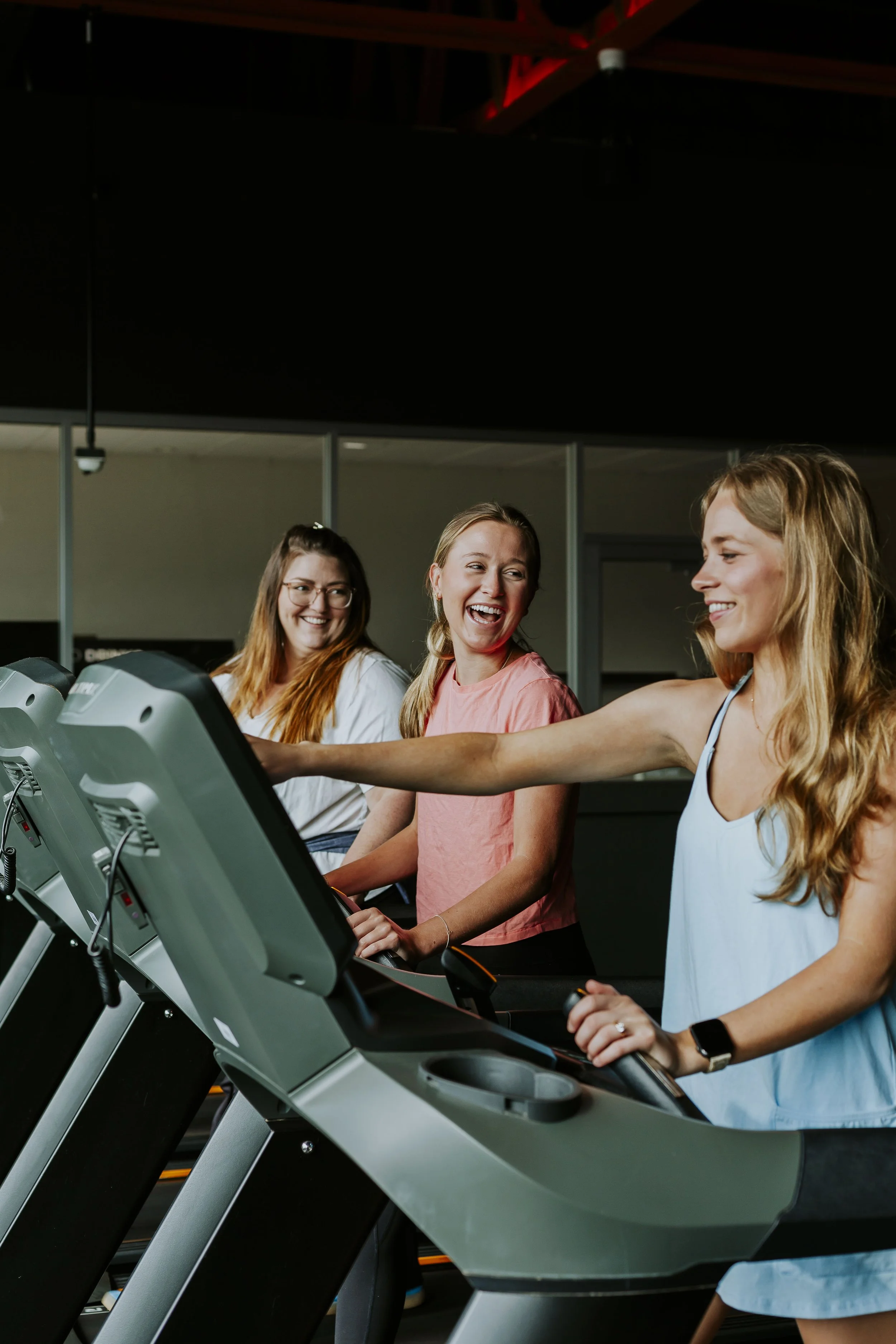 Three women smiling and walking on treadmills in a gym.