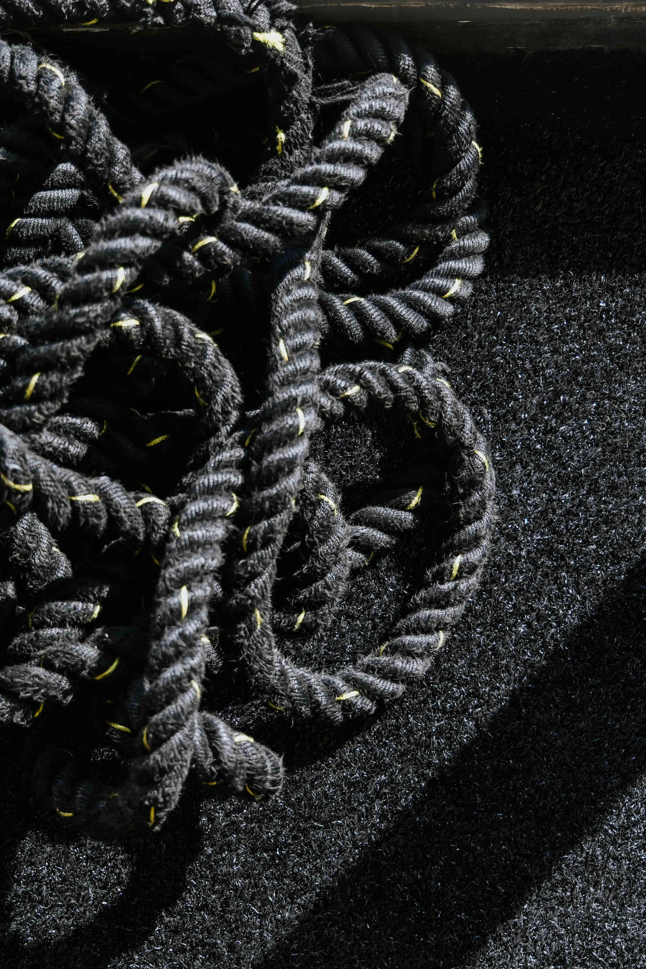 Close-up view of black ropes with yellow accents intertwined against a dark textured background.