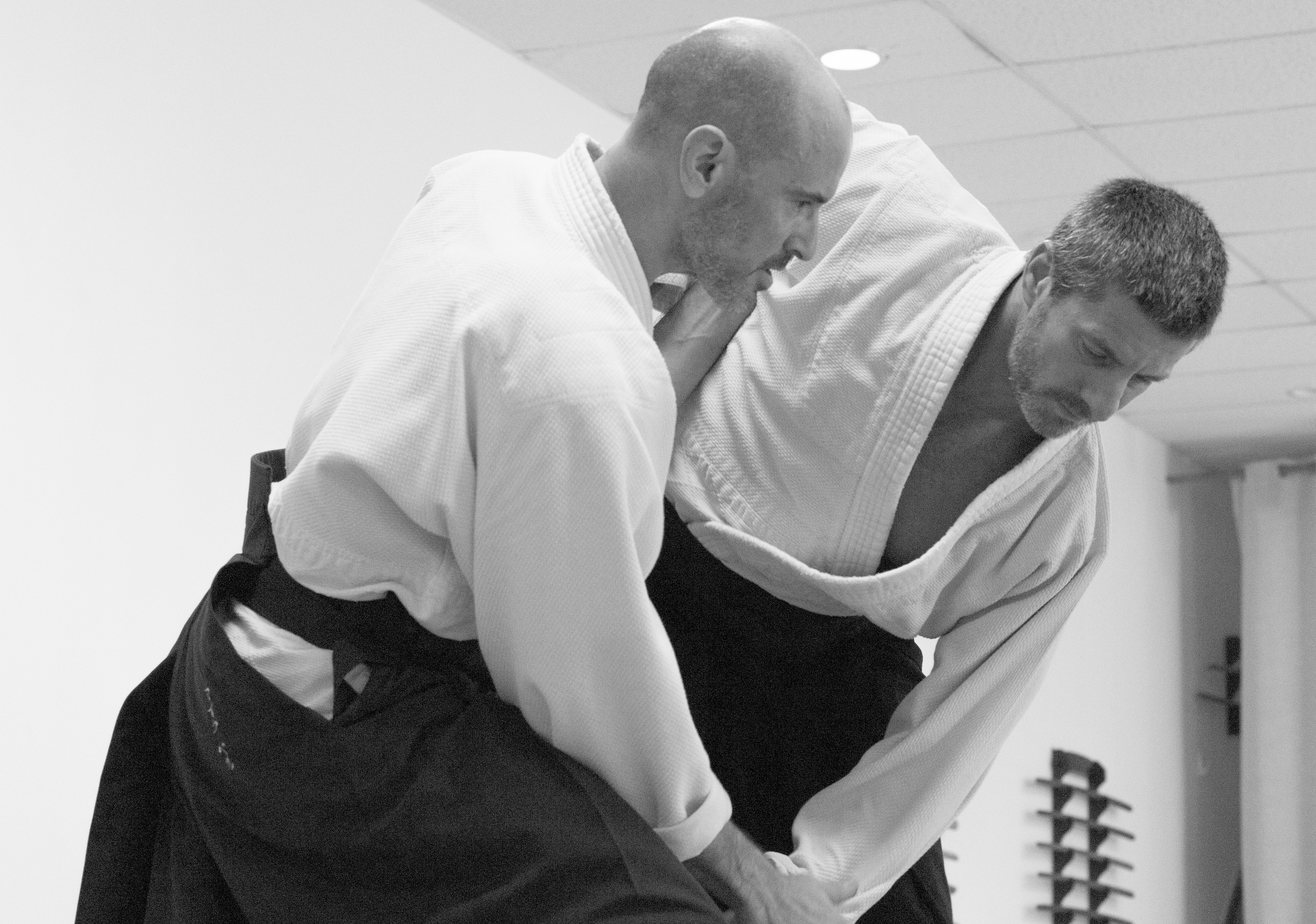 Two martial artists practicing Judo in a dojo, one in a white gi throws the other, who also wears a gi, on a padded mat.