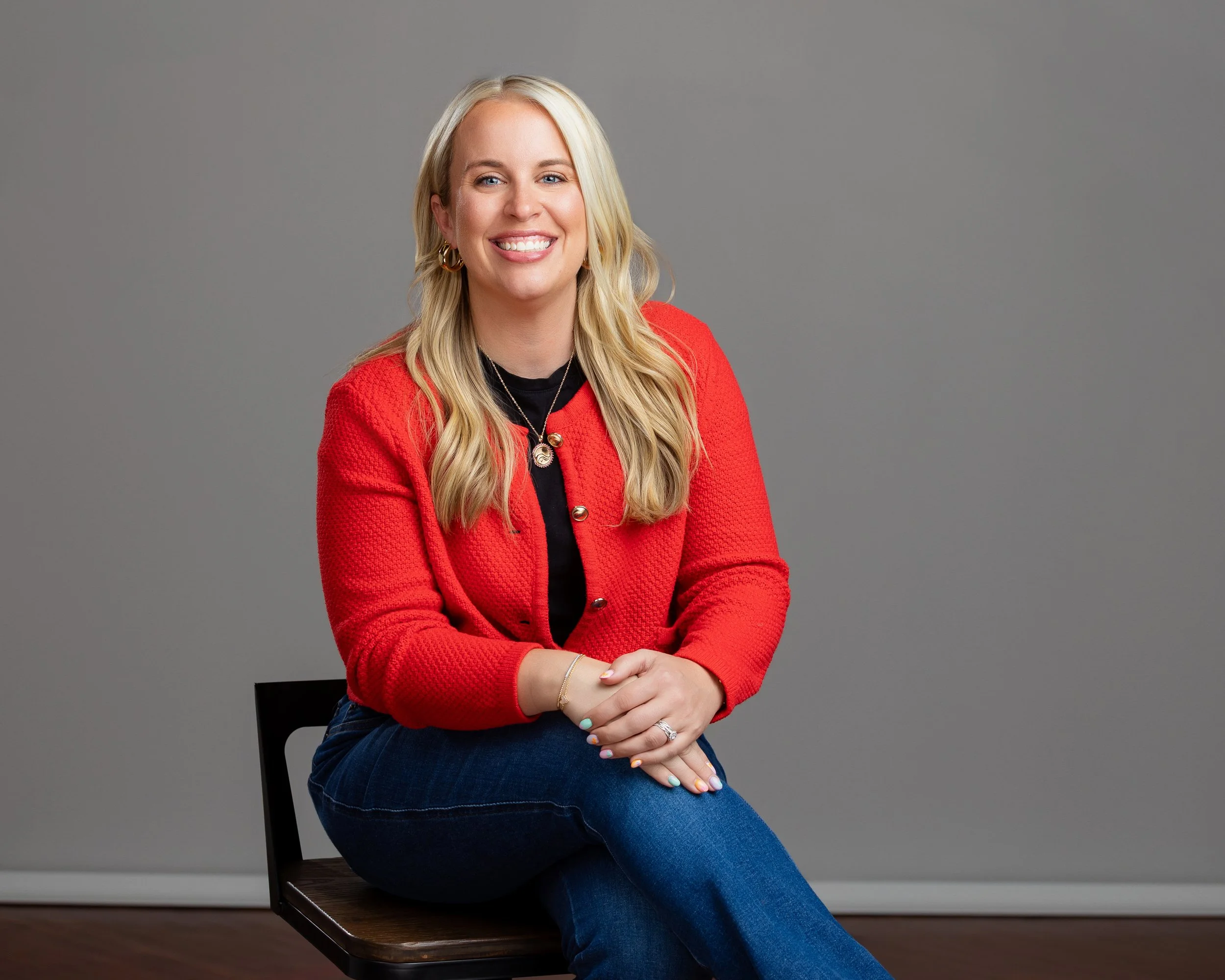 Taylor Ferretti wearing red cardigan sitting with arms folded in her lap