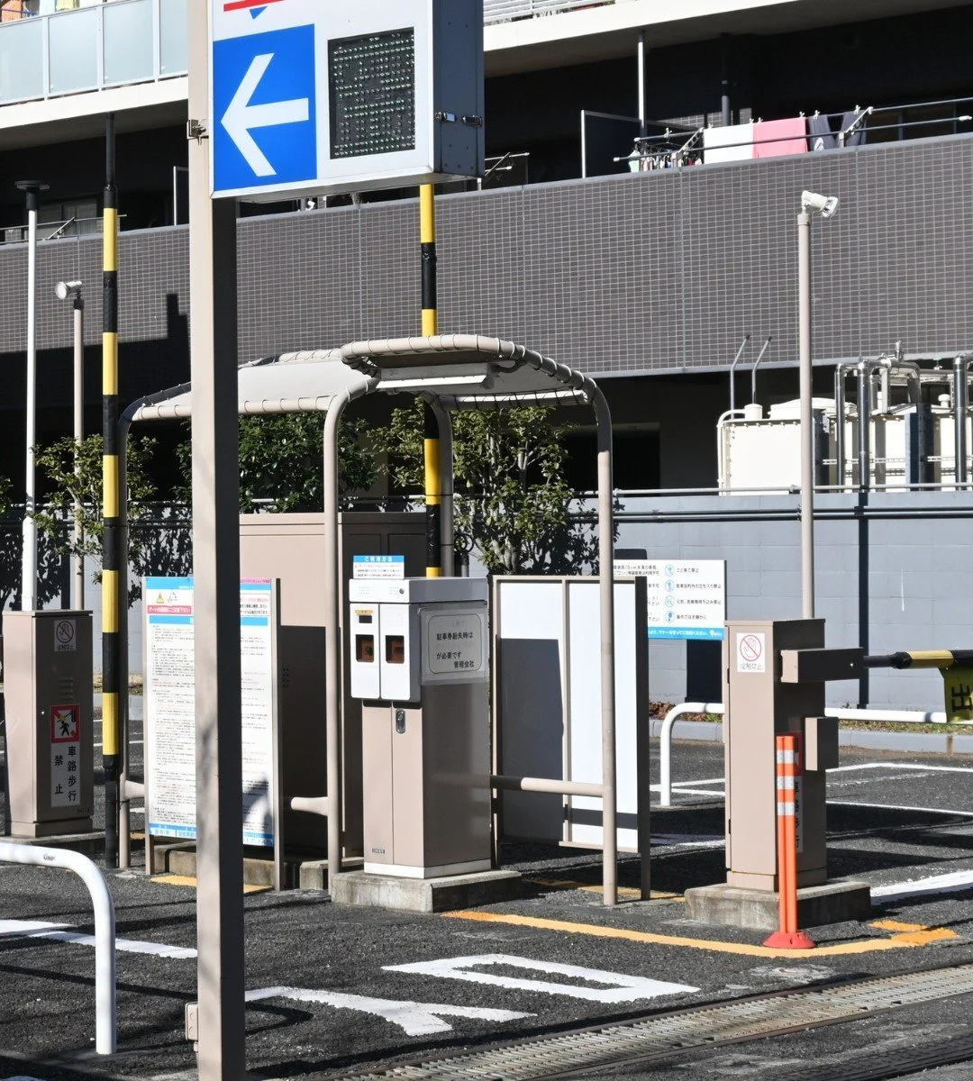 A parking entrance with a payment kiosk and a barrier gate, signage, and parking lot markings.