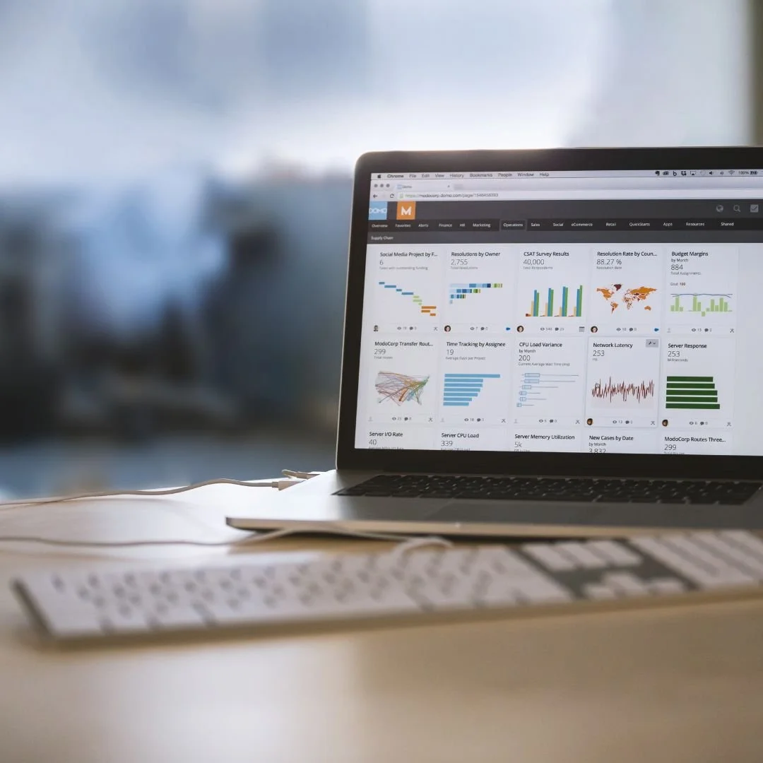 A laptop on a desk displaying various data charts and graphs on its screen.