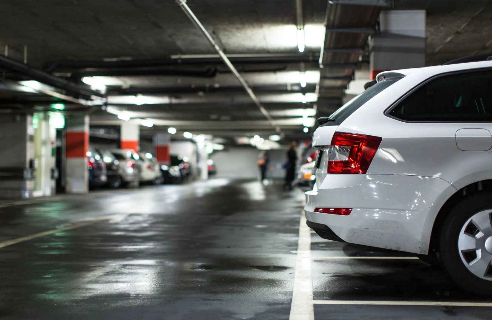 A white SUV parked in an indoor parking garage with other cars and a few people in the background.