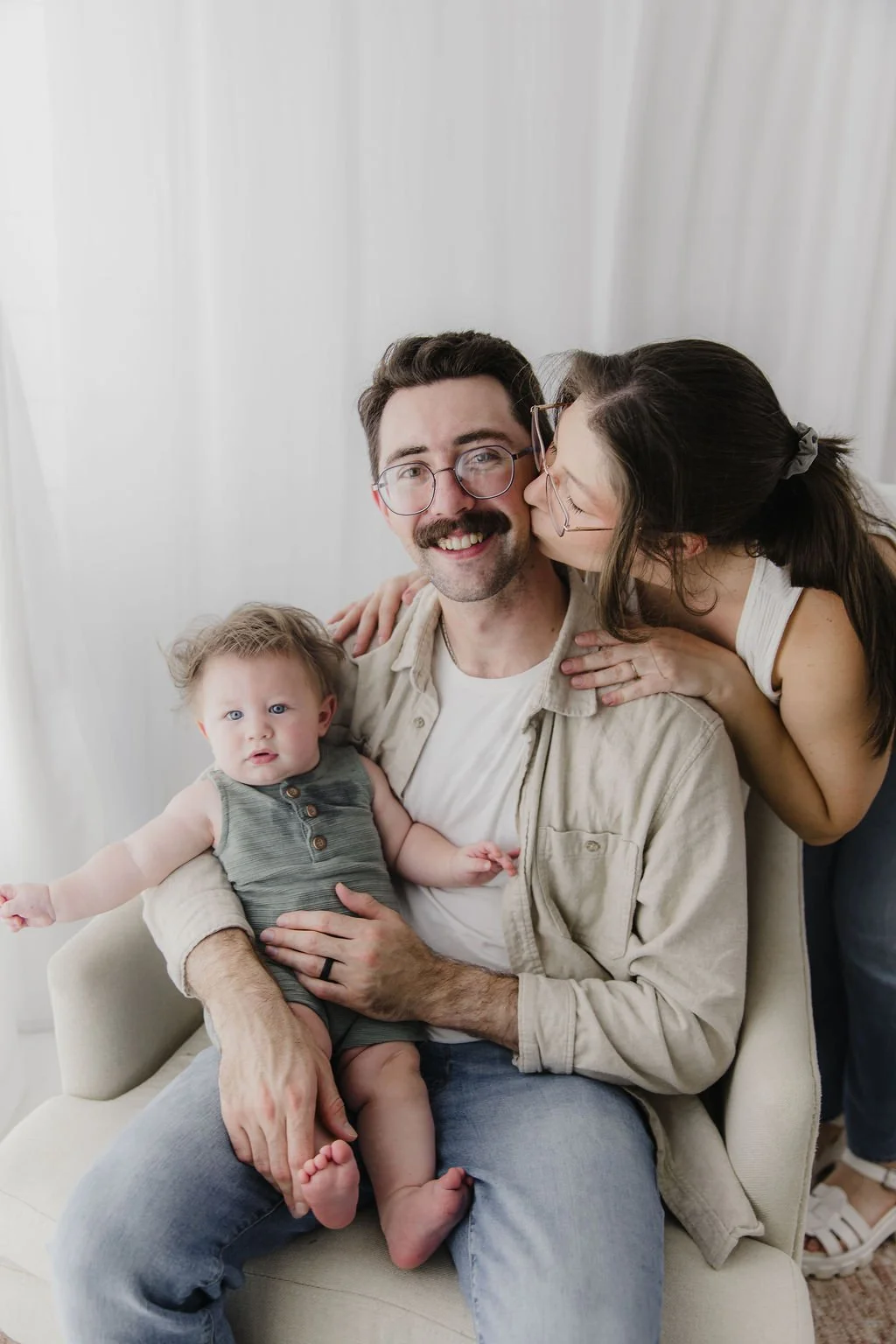 A cheerful family of three, with a young child, in a bright indoor setting.