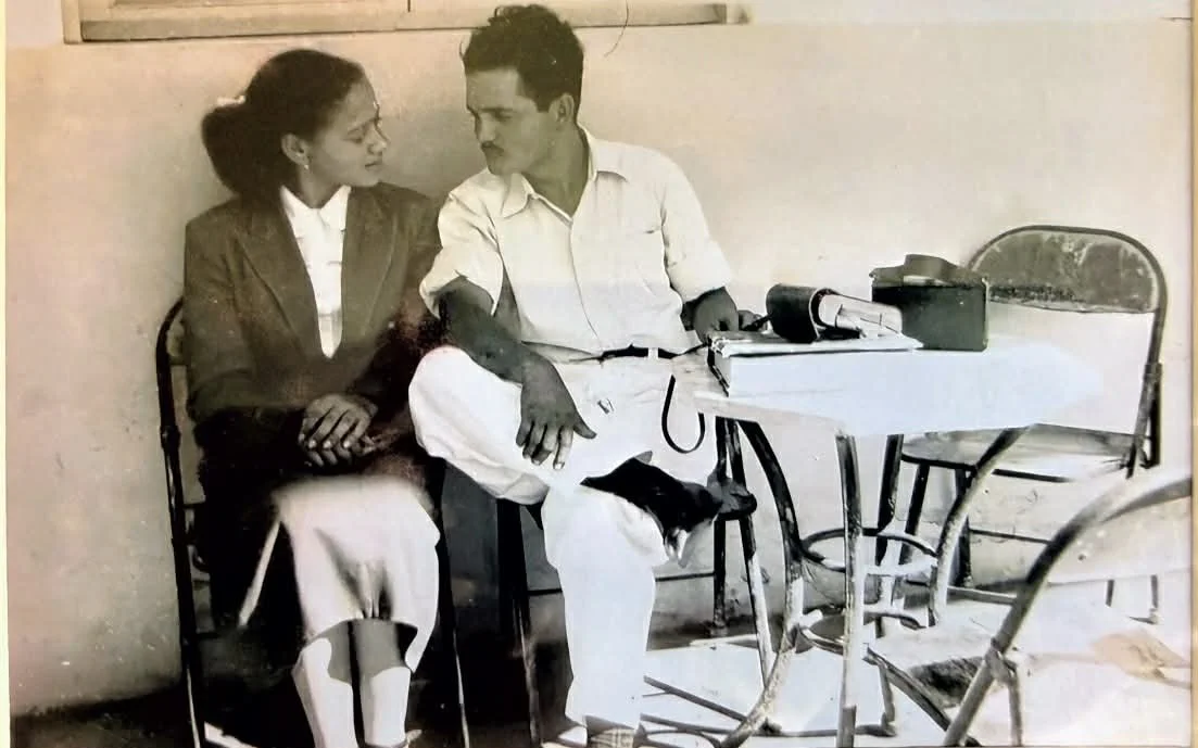 A black and white photo of a woman and a man sitting closely at a table, engaged in conversation.