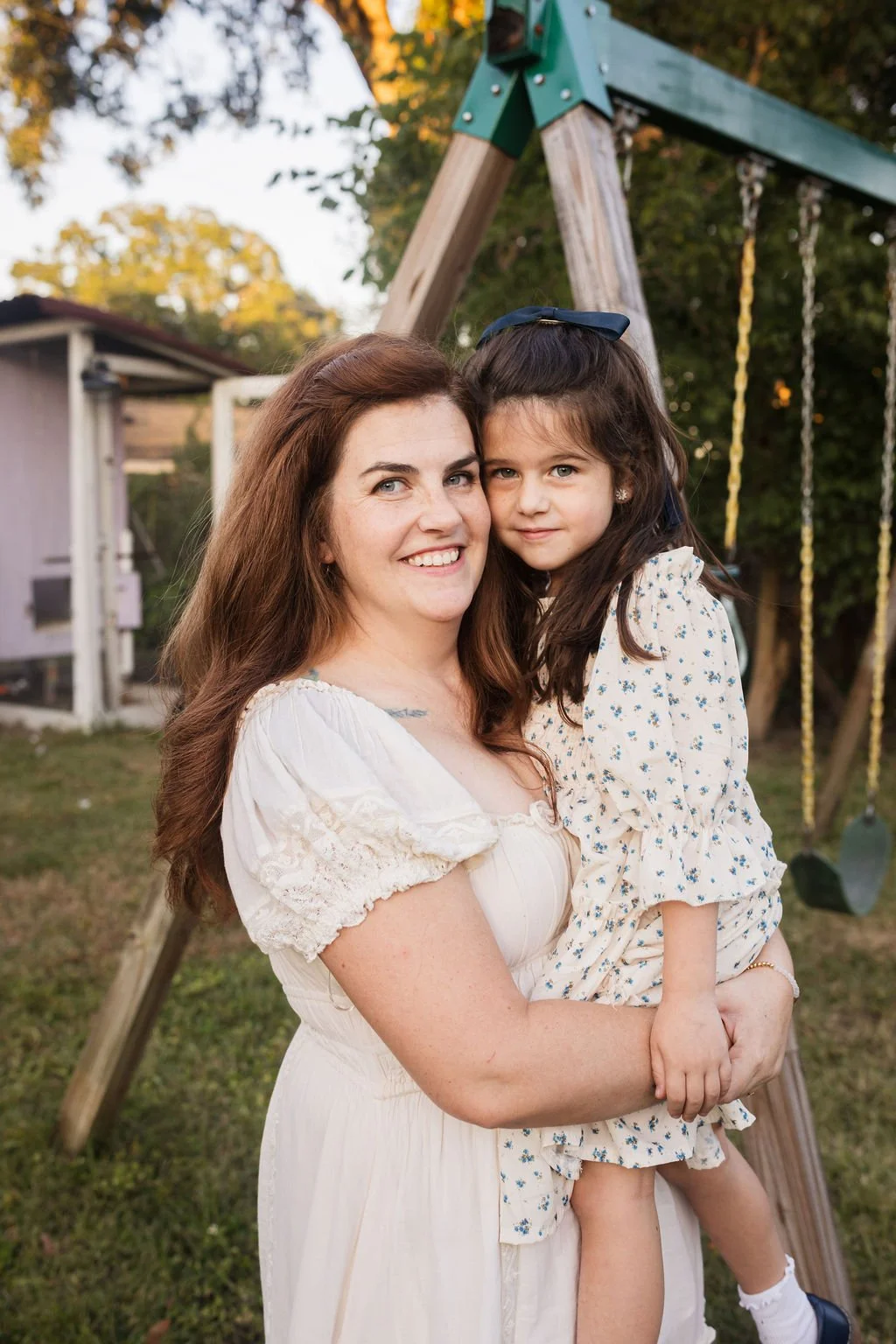 A woman holding a young girl on her hip outdoors near a playground swing set during daytime.