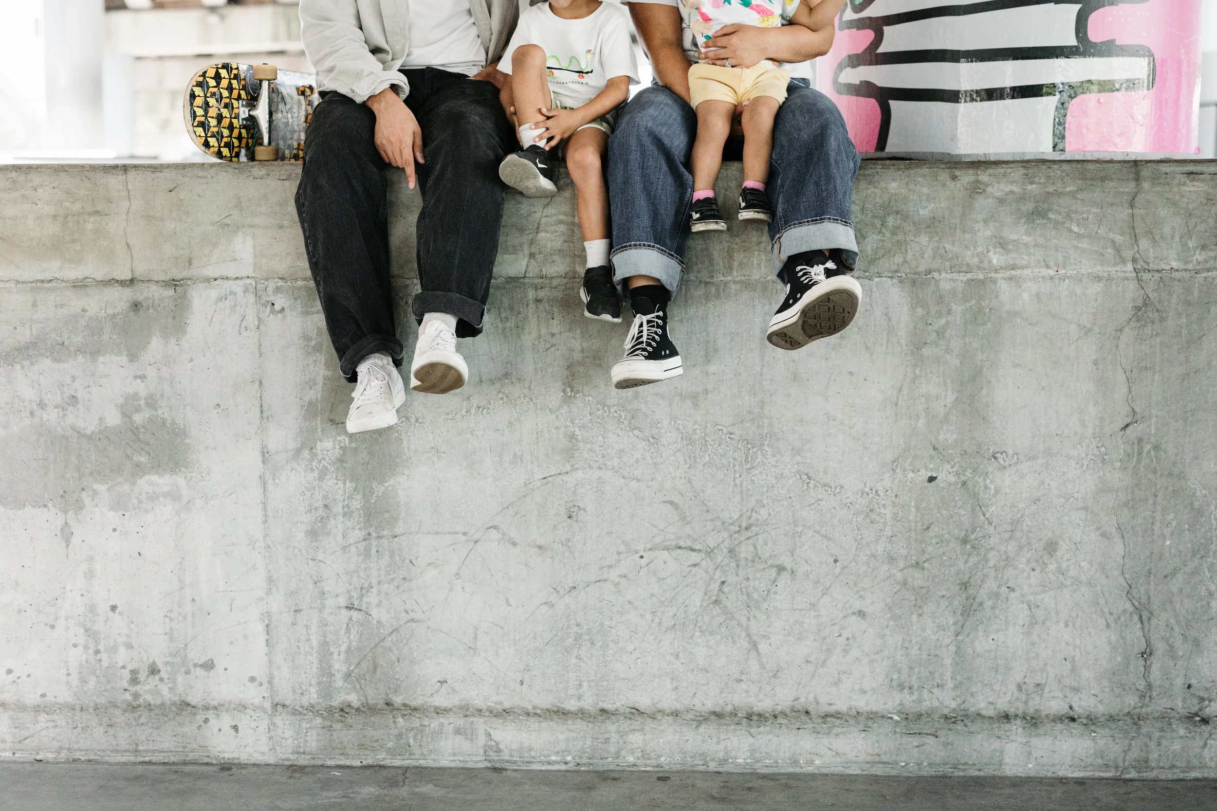 People sitting on a concrete ledge, with their legs hanging down. They are wearing casual clothes and sneakers.