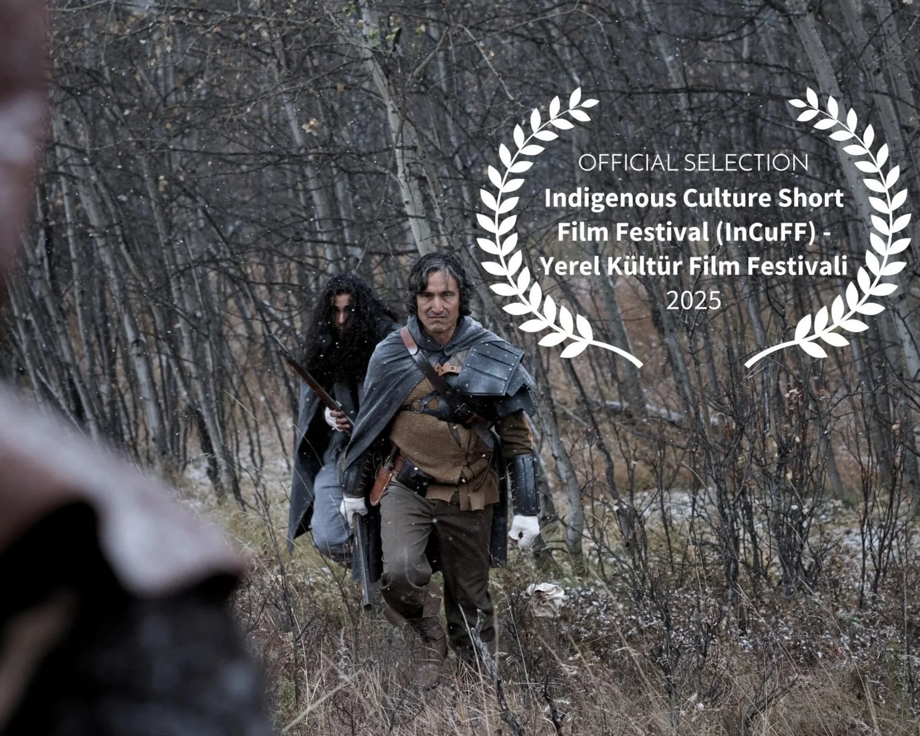 Scene from H&HA showing two people in fantasy-style costuming walking through a forest, one man with armor and one with a rifle, with an award laurel and text overlay recognizing official selection at an indigenous culture film festival in 2025.