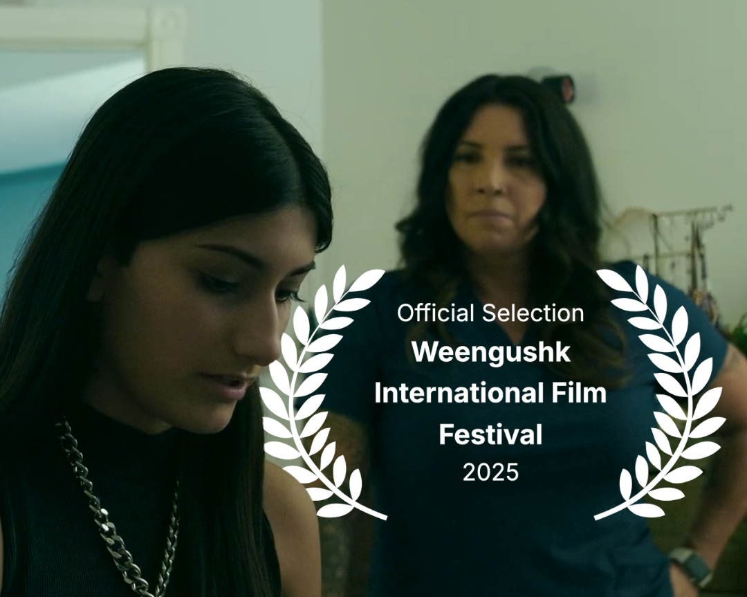 Scene from Immortal Embrace showing two women, one younger with dark hair looking down, the other older looking on, in an indoor setting. Overlaid laurel  indicates Official Selection Weengushk International Film Festival 2025.