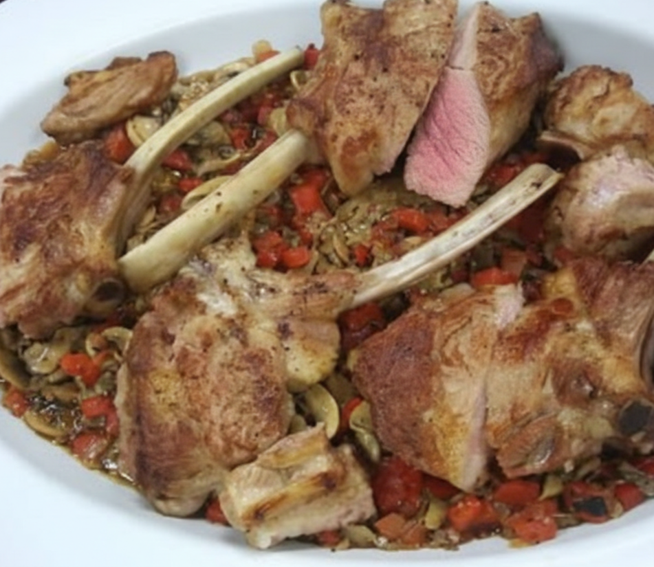 Lamb chops served over a bed of diced vegetables and pasta in a white dish.