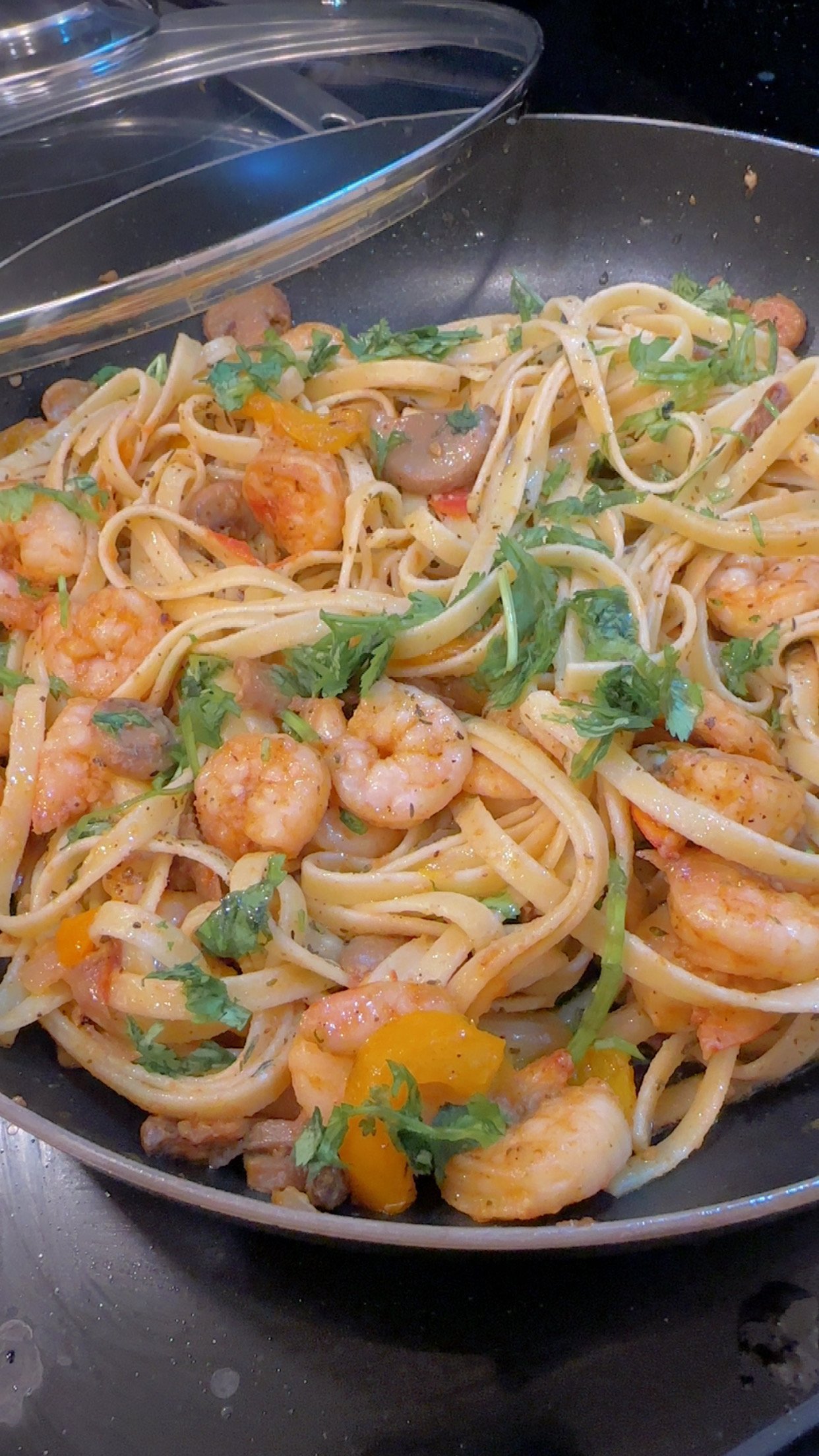 Shrimp and pasta with herbs and vegetables in a black skillet.