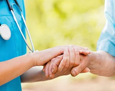 A healthcare professional holding a patient's hand outdoors.