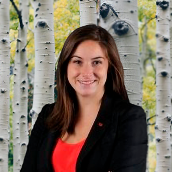 Katherine Richards smiling in a professional headshot, wearing a black blazer and red top, with a blurred tree background.