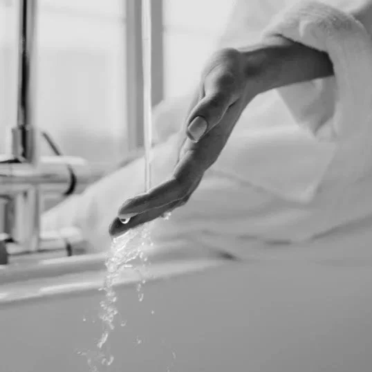 A hand with a ring on the finger dangles above a sink, with water dripping from the fingers.
