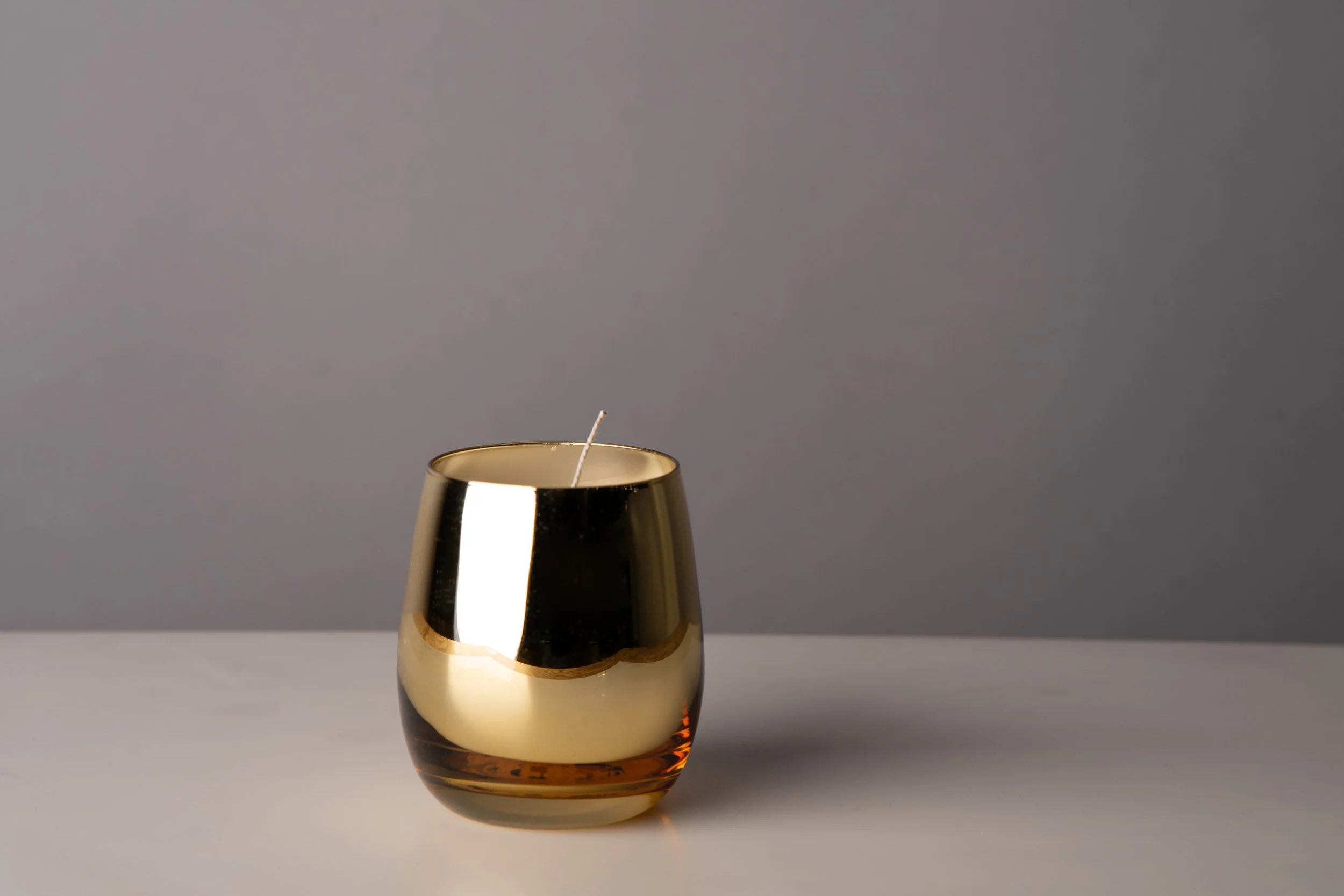 A lit candle in a metallic holder placed on a bathroom sink counter.