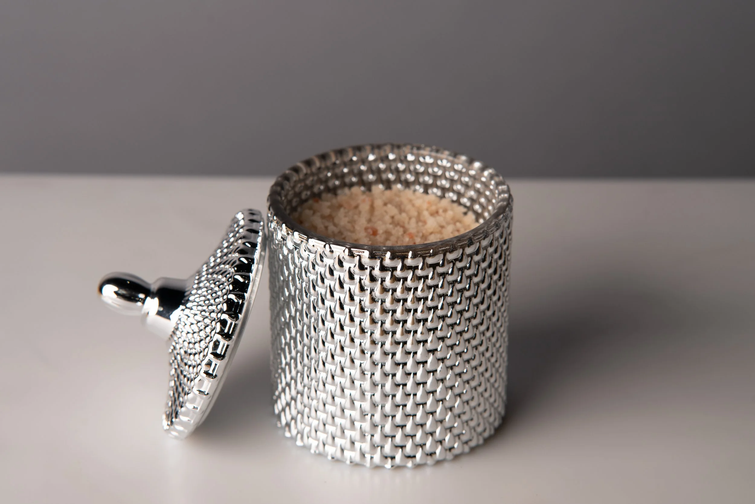 A silver, textured sugar shaker with a small shovel placed in front of it, set against a dark background.