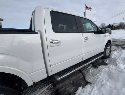 Passenger side of a white Ford F-150 with chrome handles and a silver running board.