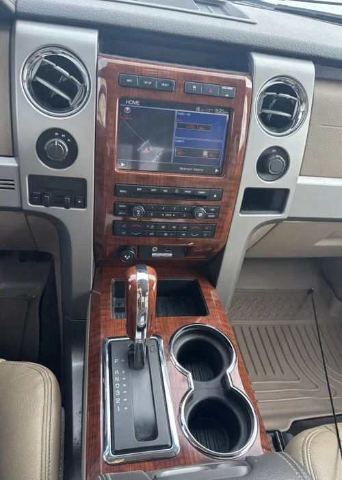 Center console of a Ford F-150 featuring a wood-grain finish, infotainment screen, gear shifter, and dual cup holders.