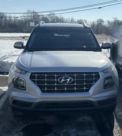 Frontal view of a silver Hyundai Venue showing its prominent mesh grille and Hyundai logo in a snowy outdoor setting.