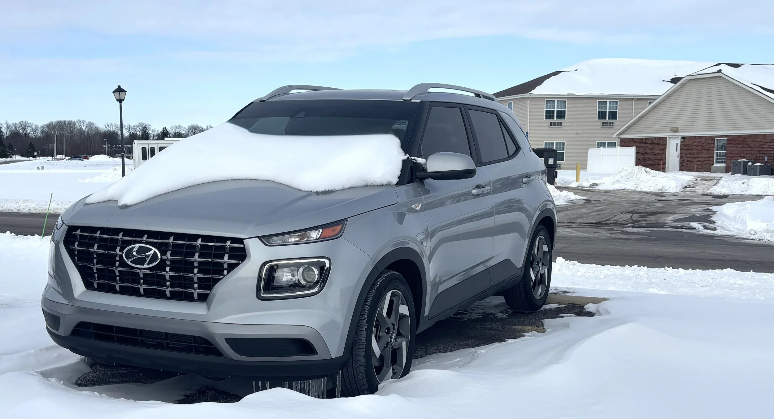Front three-quarter view of a silver Hyundai Venue SUV parked in a snowy lot with snow partially covering the windshield.