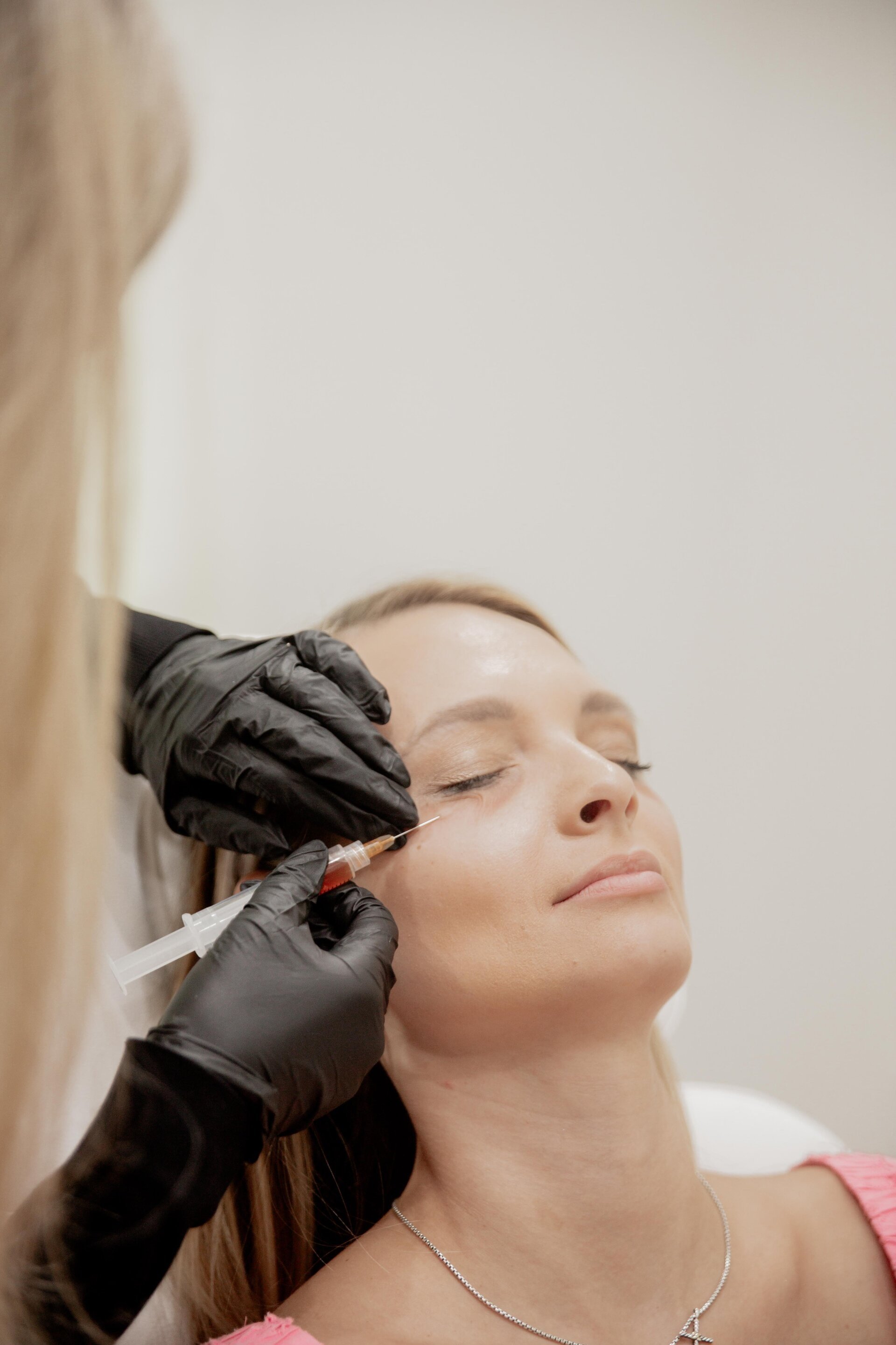 A woman receiving a cosmetic injection in her face while lying back with eyes closed.