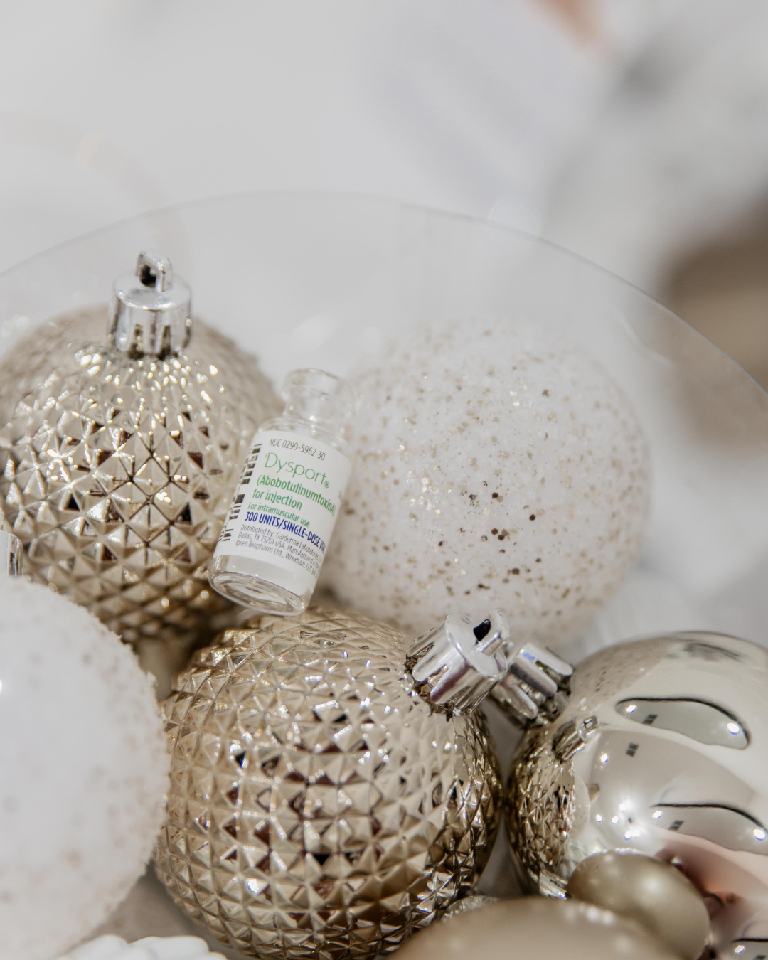 Close-up of decorative Christmas ornaments, including gold and silver baubles, and a vial of Dysport injectable medication.