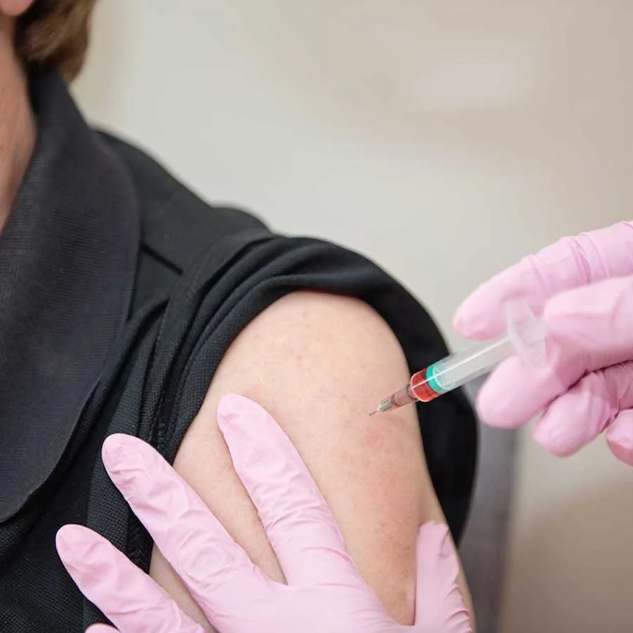 Person receiving a shot in their upper arm administered by healthcare professional wearing pink gloves.