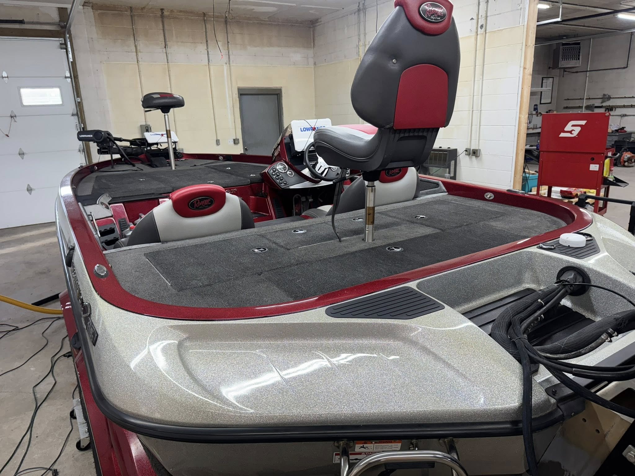 A red and grey fishing boat inside a garage, showing the cockpit with seats and steering wheel.