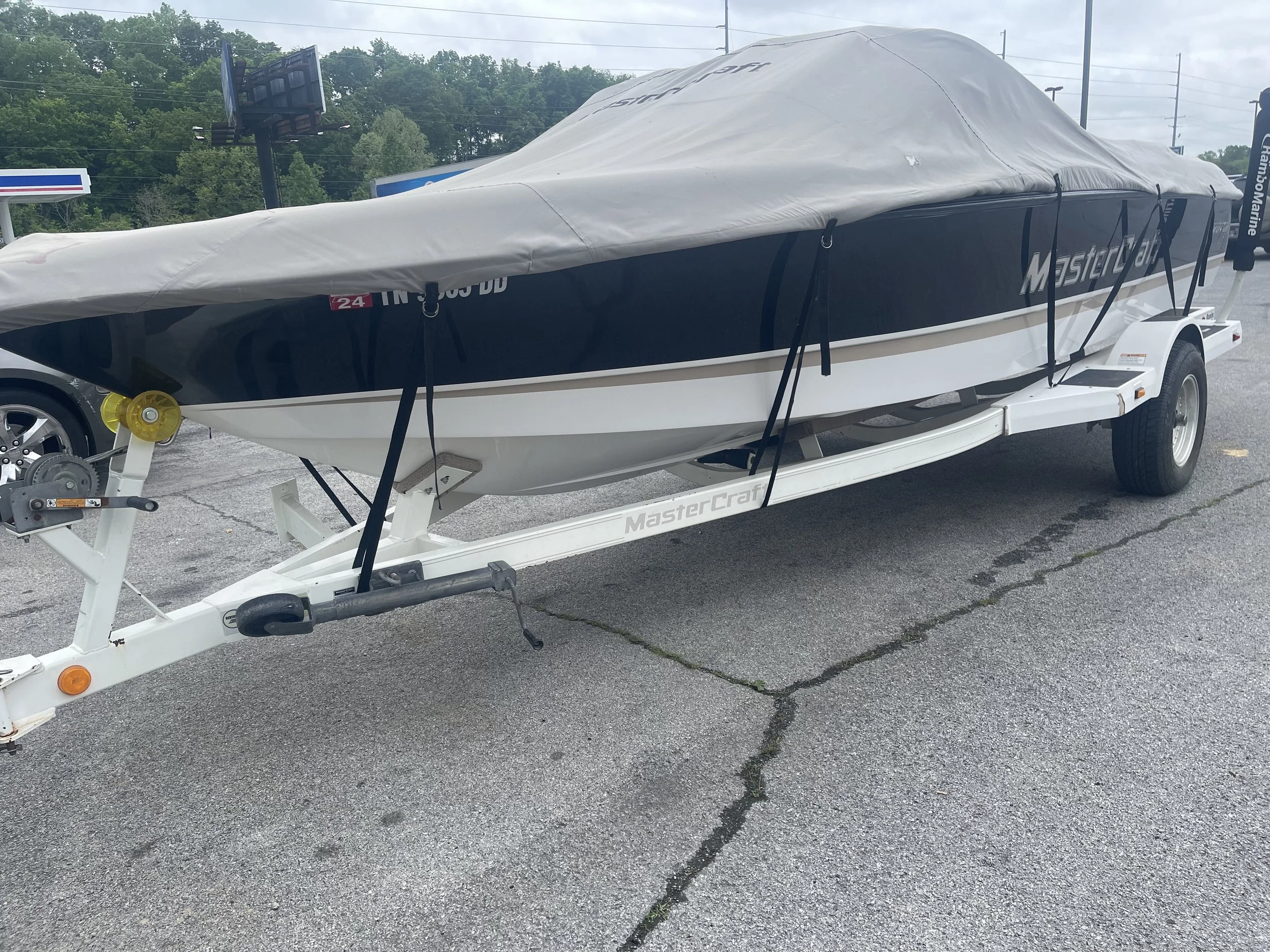 A speedboat on a trailer covered with a grey tarp parked on a gravel lot.