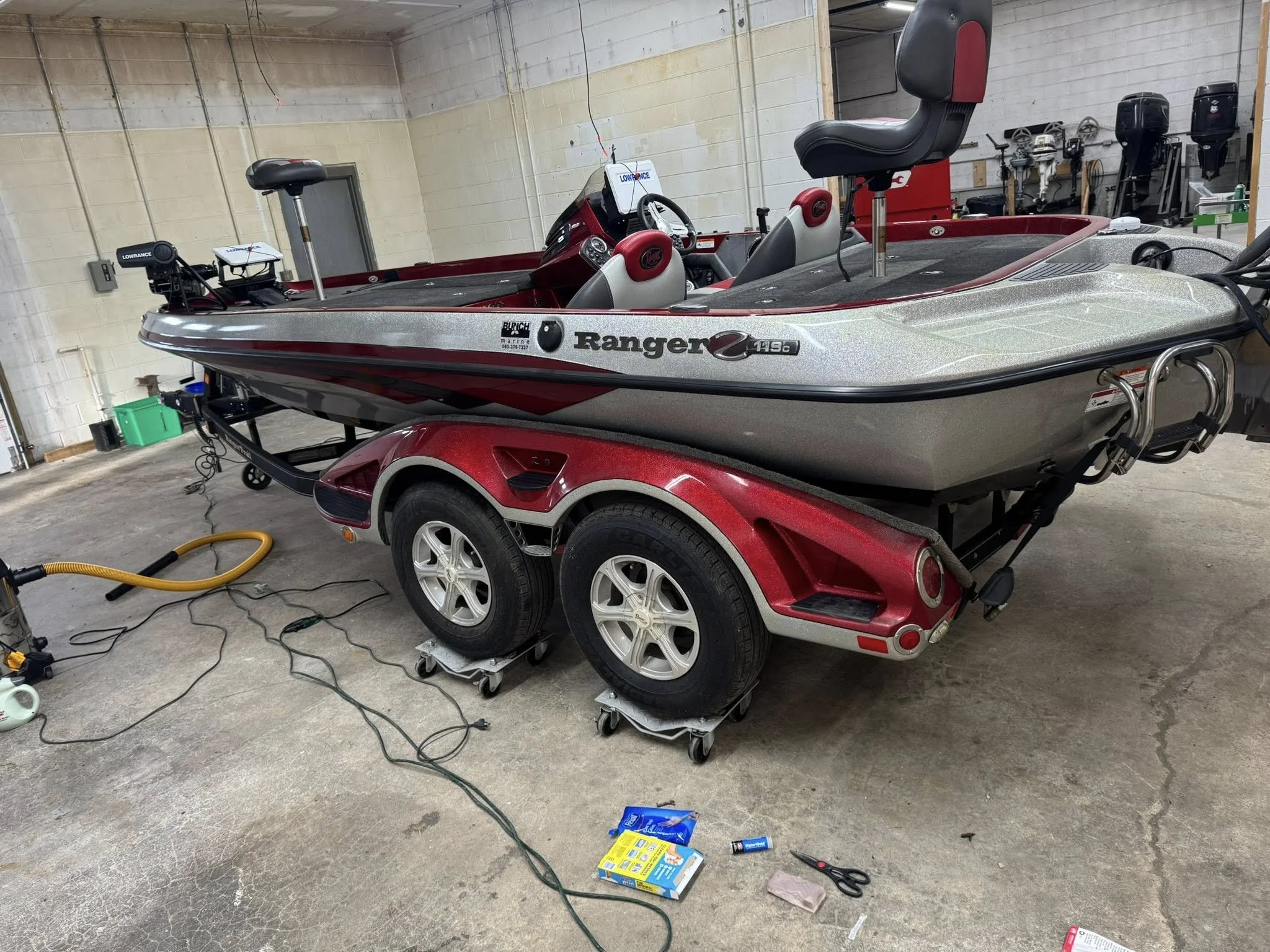 A Ranger bass boat on a red trailer inside a garage or storage space with tools and equipment visible in the background.