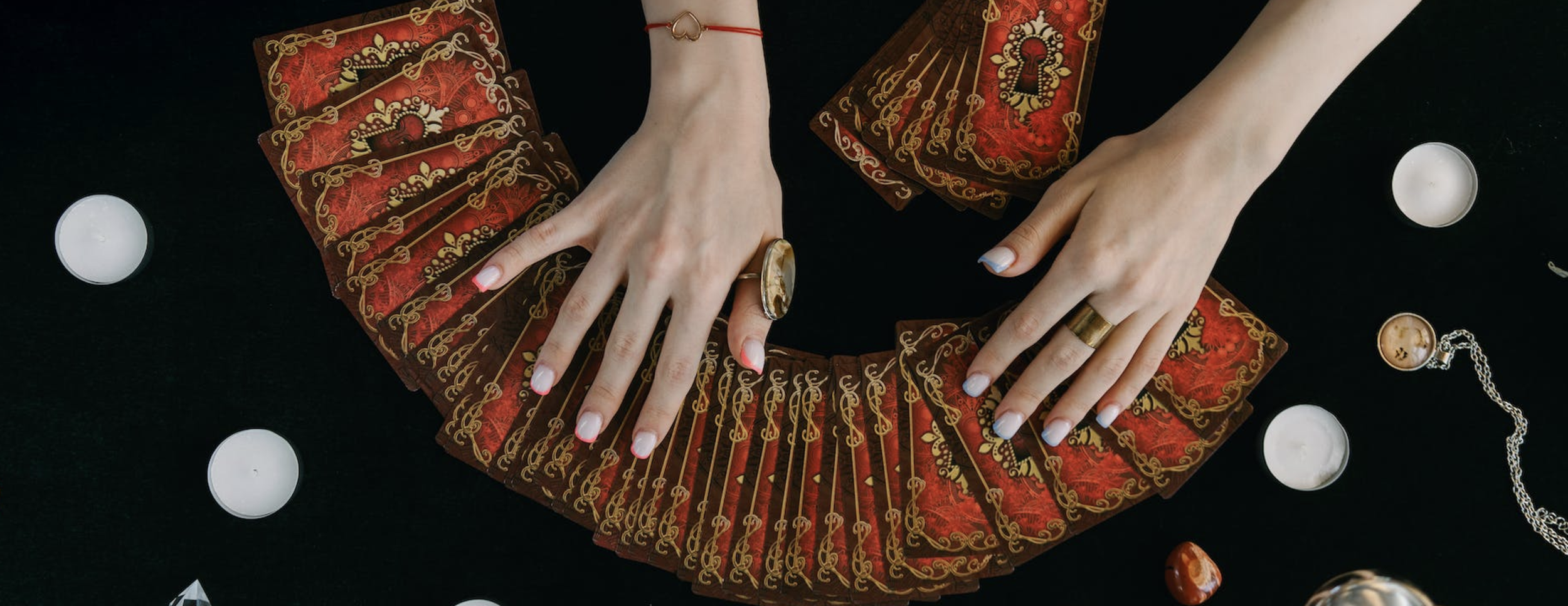 red and gold tarot cards fanned out against a dark background showing two hands reaching over the cards