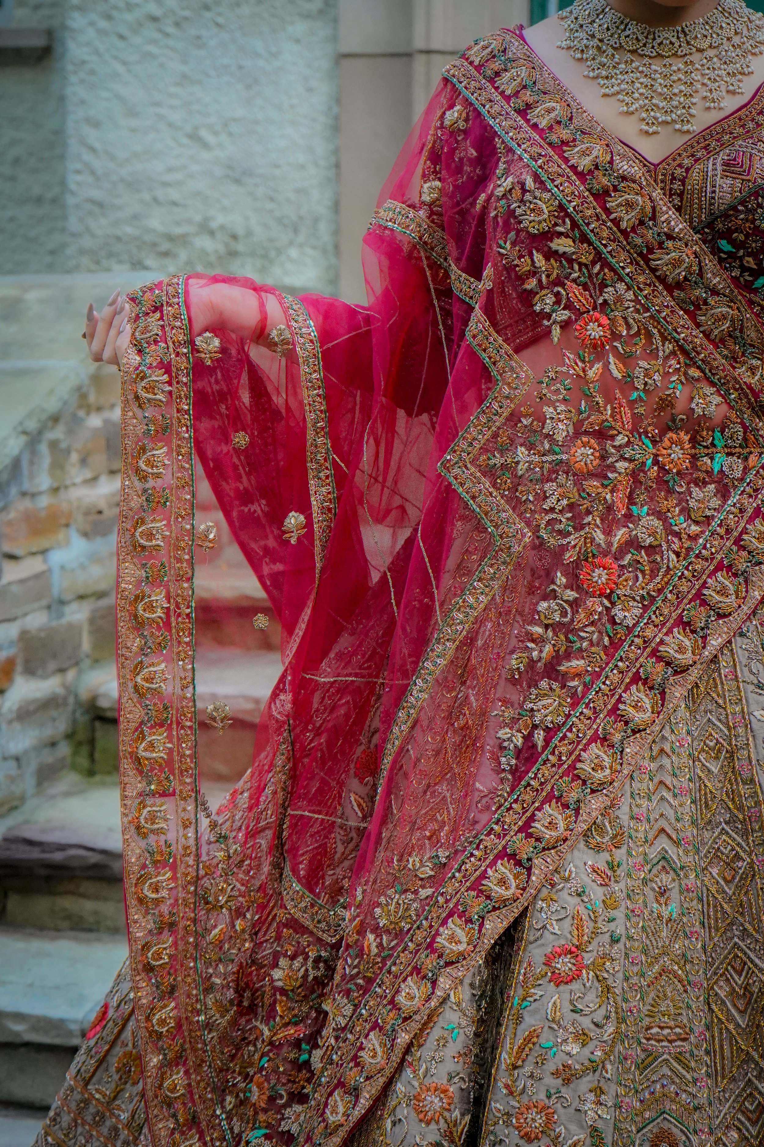 Close-up of a woman wearing a traditional, heavily embroidered pink and beige Indian saree with jewelry.