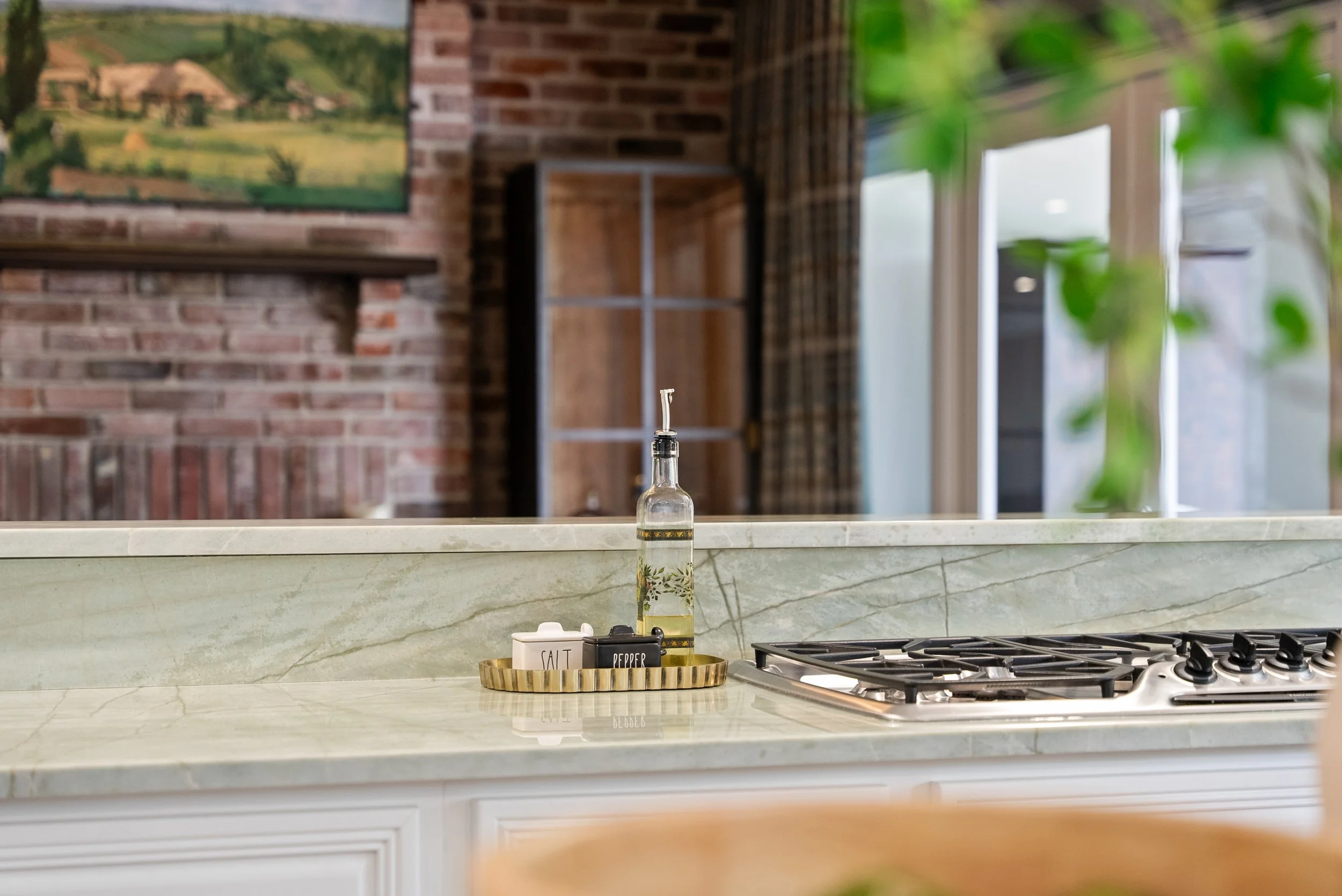 A kitchen countertop with a soap dispenser, salt and pepper shakers, and a tray, with a brick wall and a window in the background.