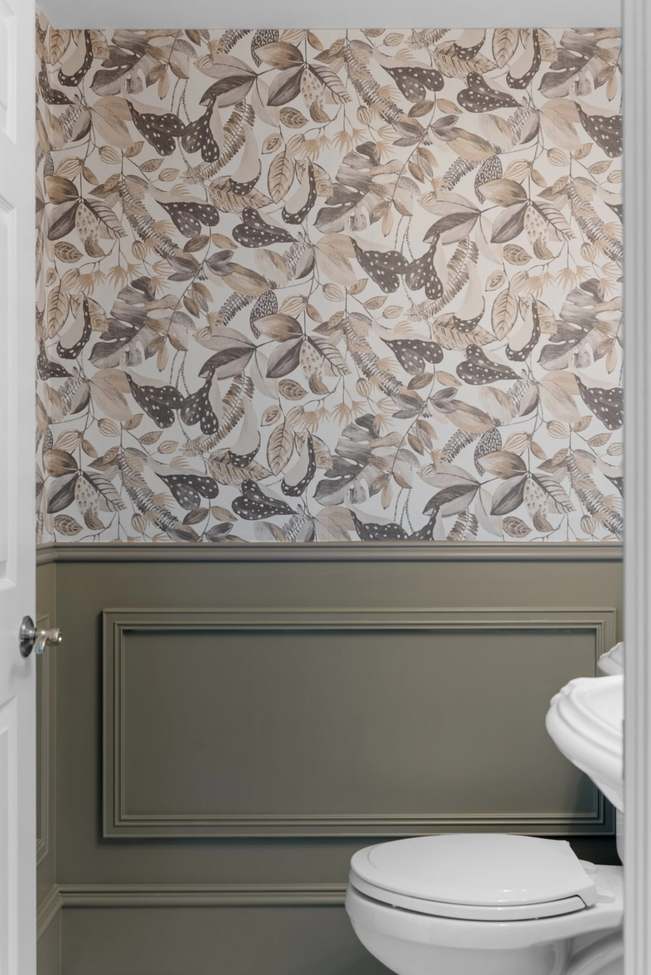 A bathroom with a decorative wall featuring a leafy and butterfly pattern, a green wainscot panel, and a white toilet