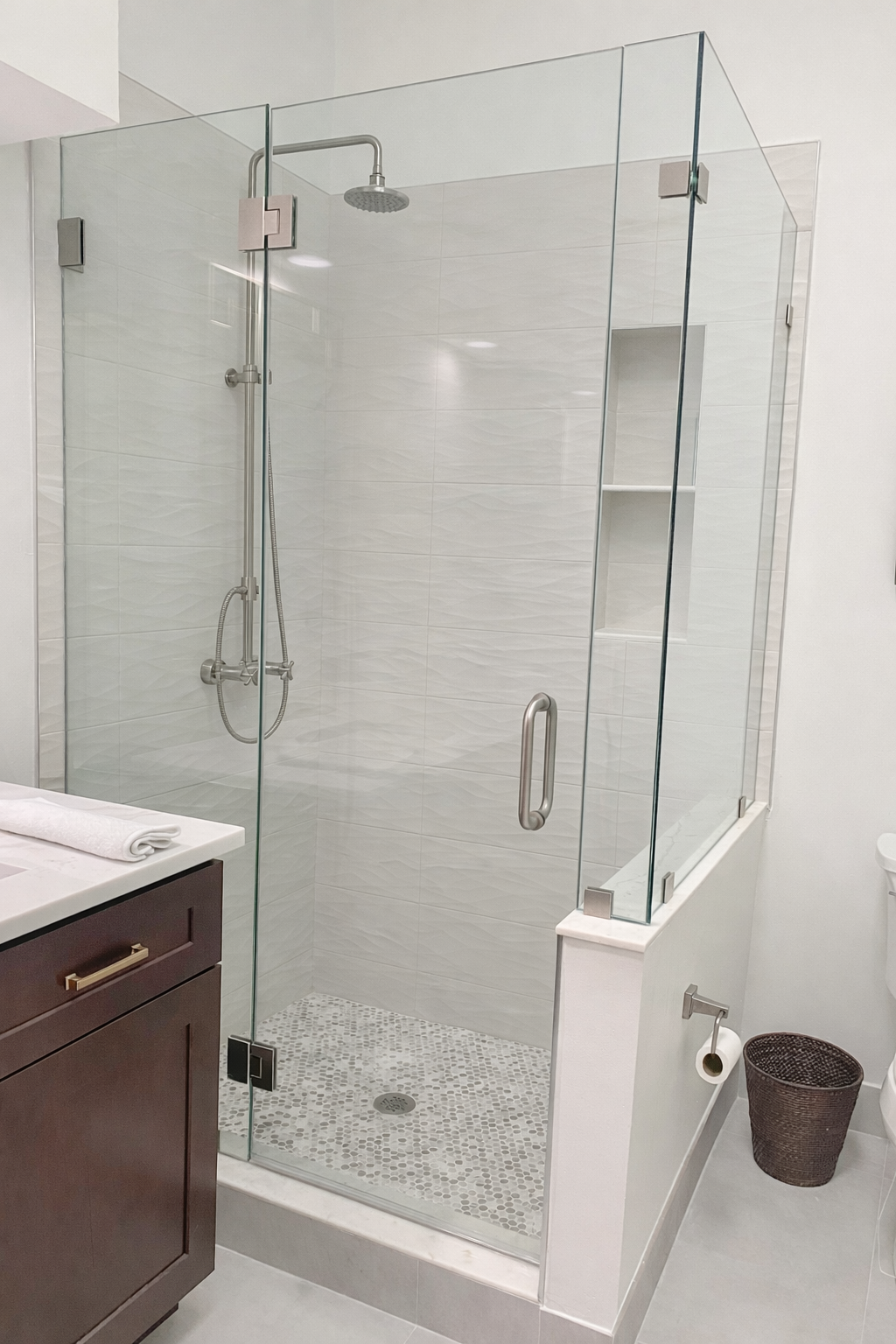 Modern glass-enclosed shower with silver fixtures, white tiled walls, pebble floor, and built-in niche, located in a contemporary bathroom.