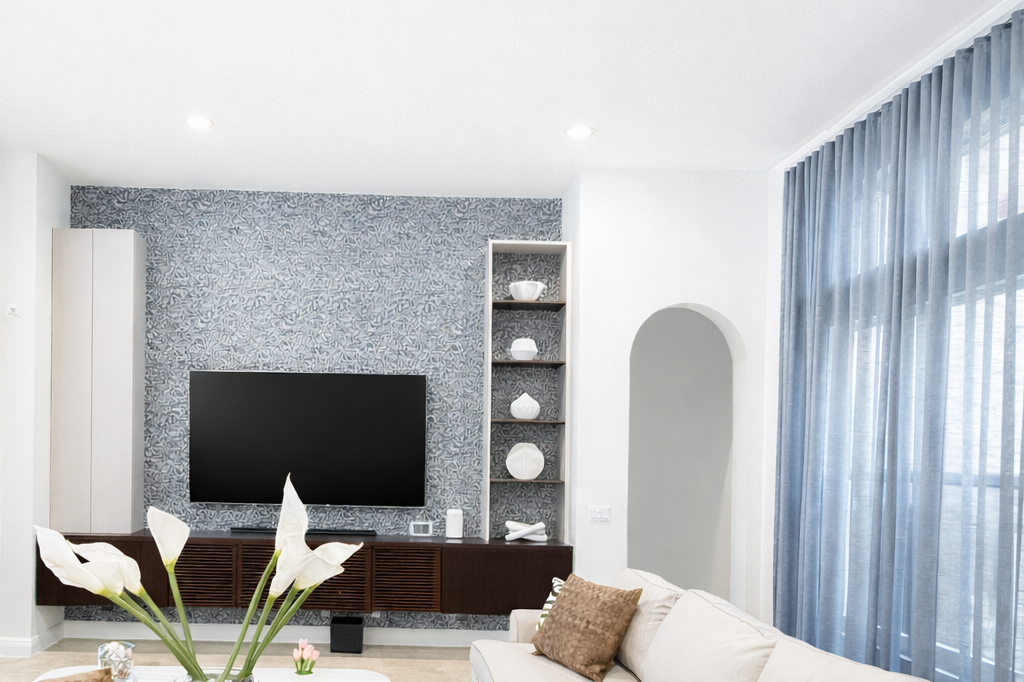 Living room with a wall-mounted TV, blue patterned accent wall, white and beige furniture, decorative vases on a wall shelf, and large windows with blue curtains.
